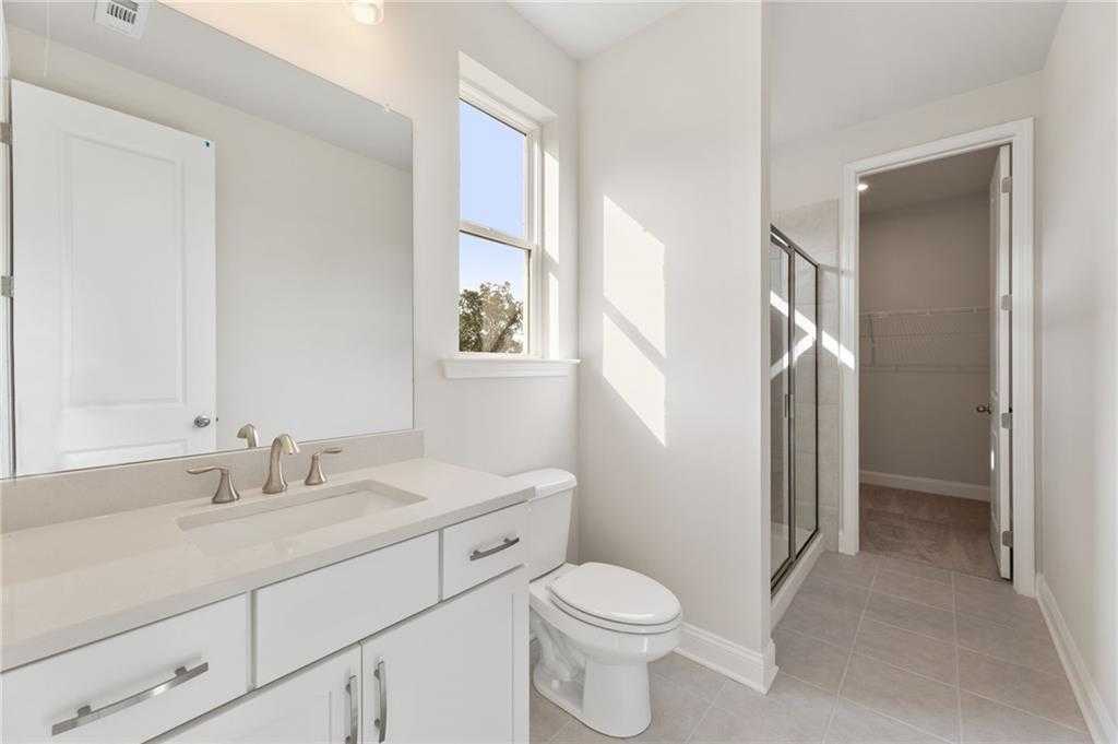 Bright bathroom with white vanity, single sink, glass shower, toilet, and window in The Hampton C by Davidson Homes, Buford, GA