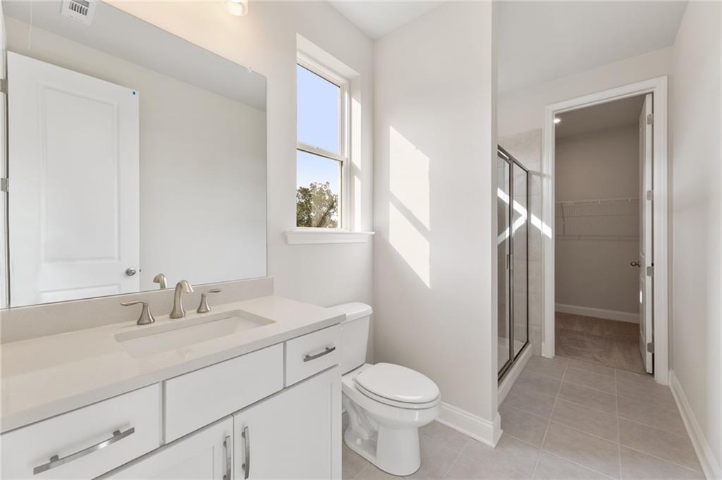 Bright bathroom with white vanity, single sink, glass shower, toilet, and window in The Hampton C by Davidson Homes, Buford, GA