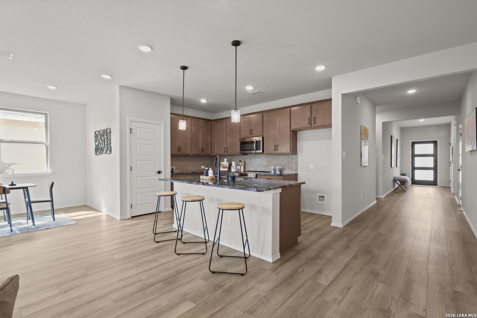 Modern open-concept kitchen with wooden cabinets, granite island, and bar stools in Davidson Homes The Daphne H, Seguin, Texas