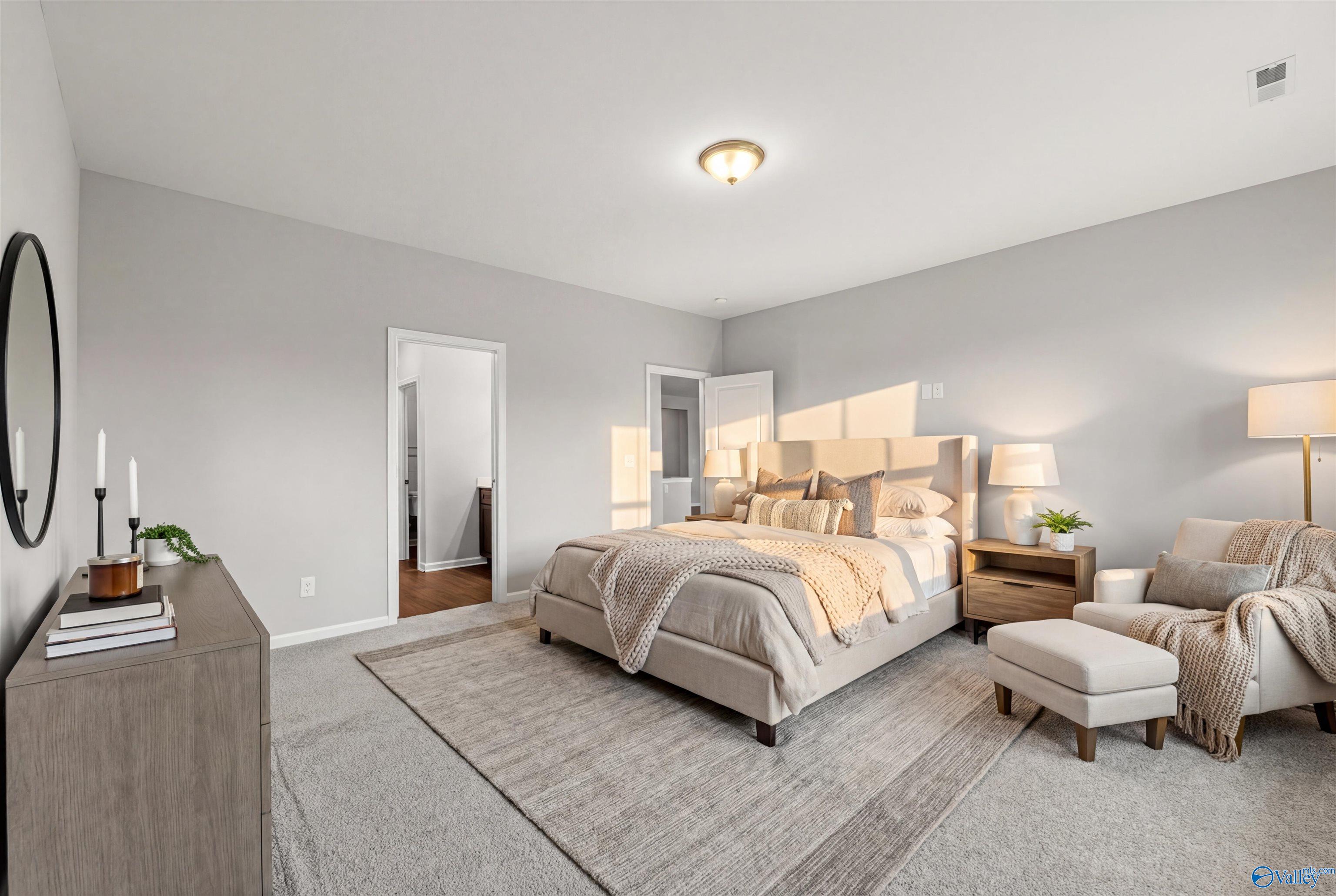 Serene master bedroom with king bed, beige linens, neutral gray walls, and accent chair in Davidson Homes The Sanctuary, Huntsville, Alabama