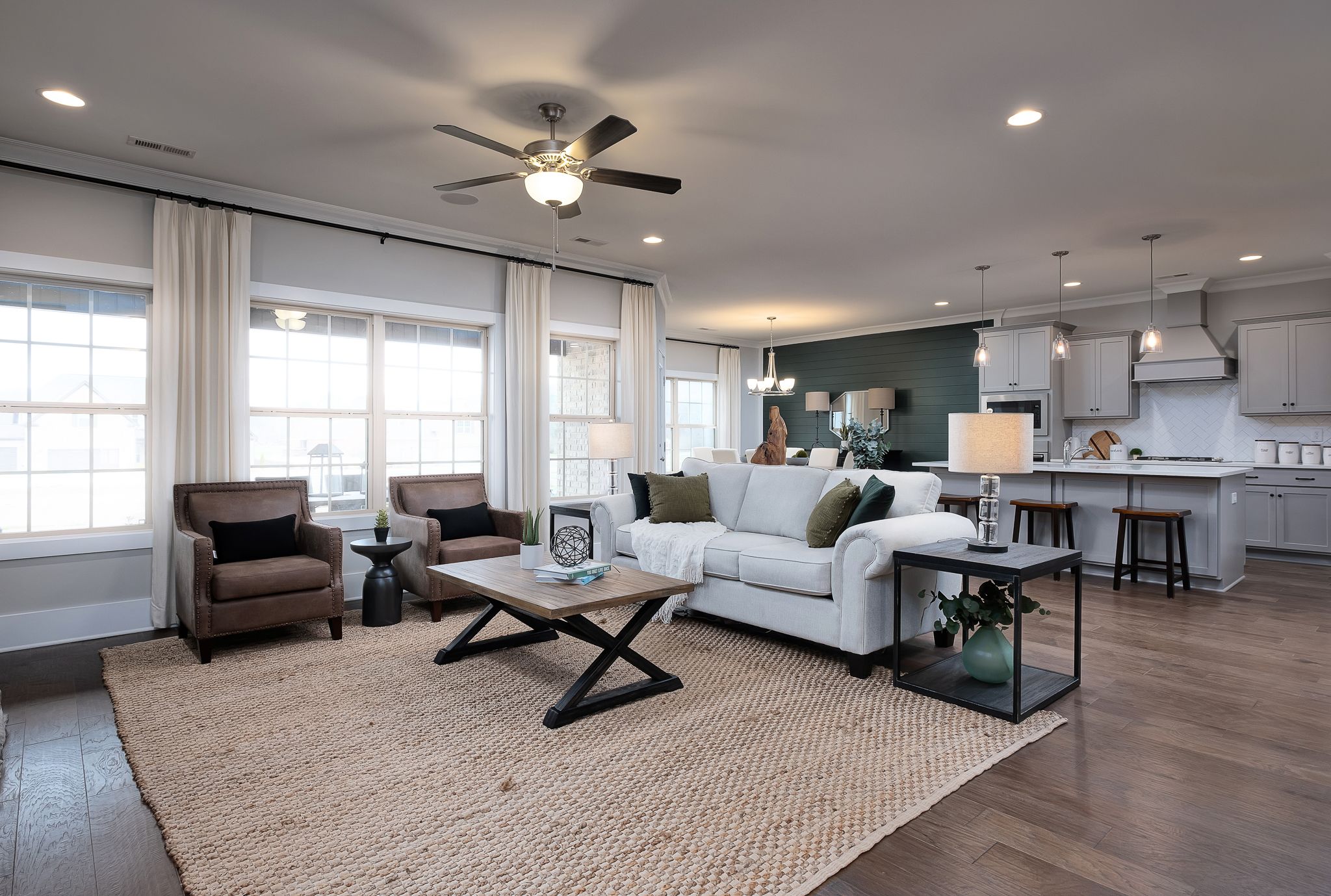 Open-concept living room at Chimney Creek in Hampton Cove Alabama with white sofa hardwood floors jute rug and modern kitchen island