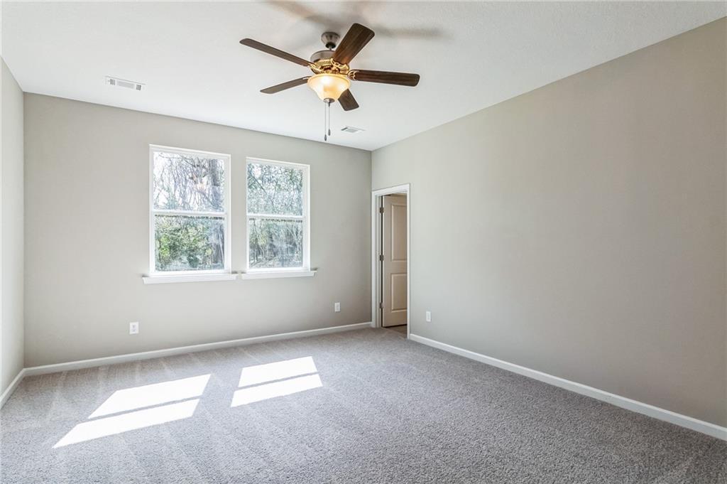 Bright secondary bedroom with ceiling fan, large sunny windows, and gray carpet in Evermore Homes The Stella, Ivy Glen, Perry, Georgia