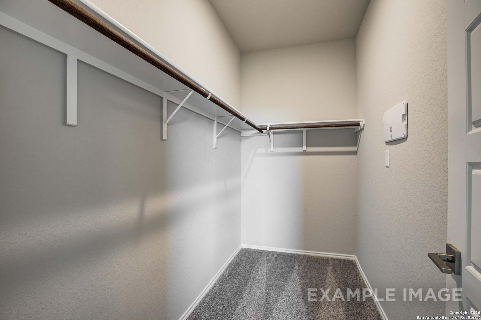 Spacious walk-in closet with wooden shelves, beige walls, and carpeted floor in Davidson Homes The Frio C, Agave, San Antonio