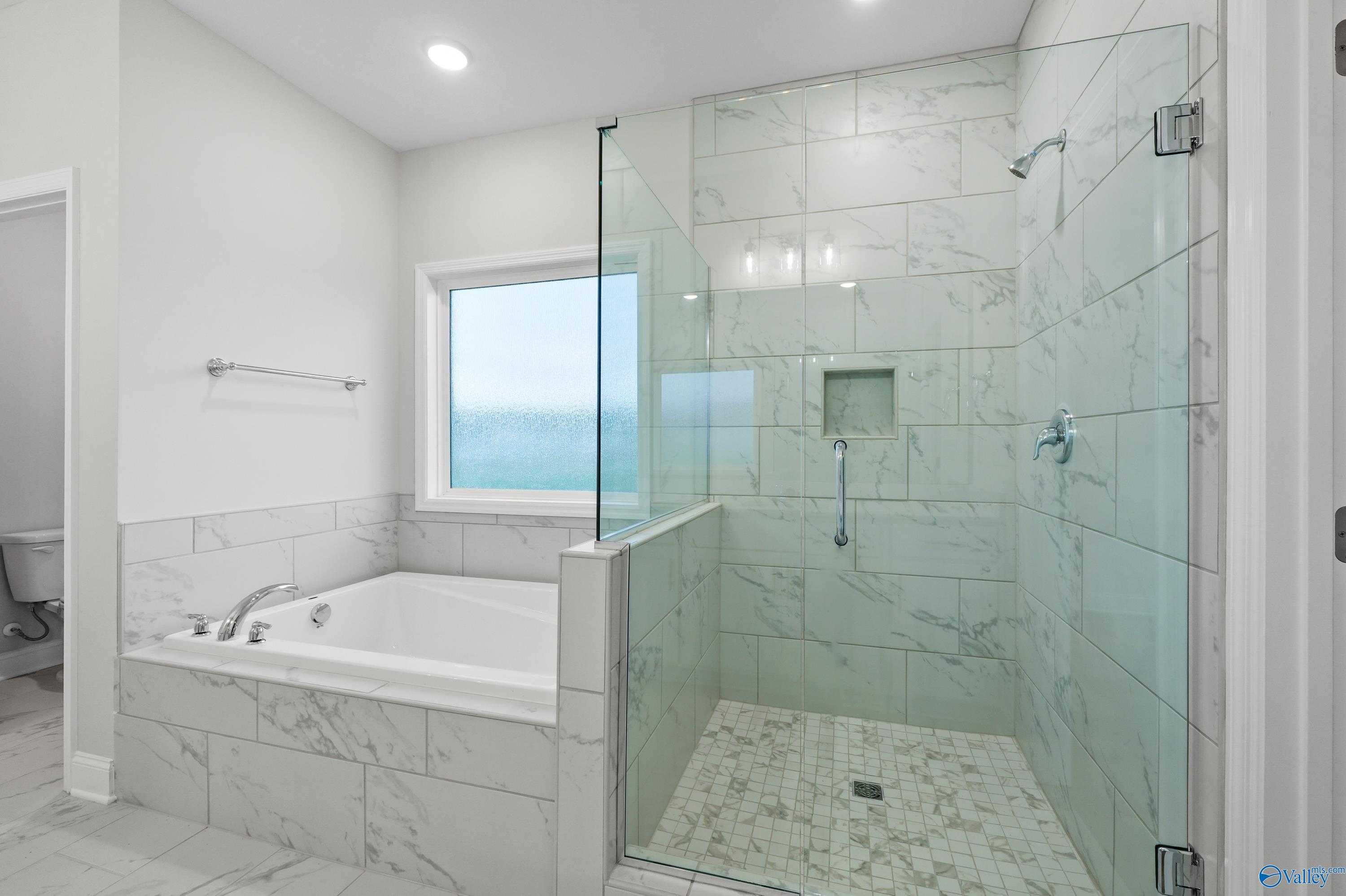 Elegant master bathroom with glass shower, green marble tiles, and freestanding tub in Davidson Homes The Lanier, Harvest, AL