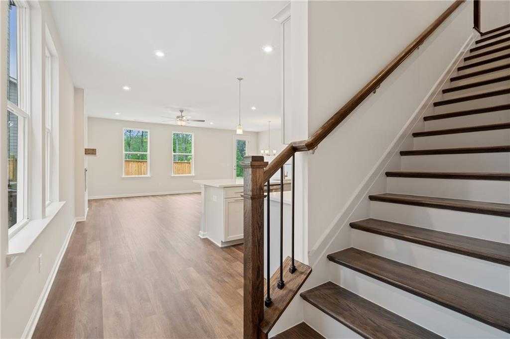 Bright open foyer with wooden staircase, hardwood floors, and kitchen island in The Cary B home, Kennesaw, Georgia