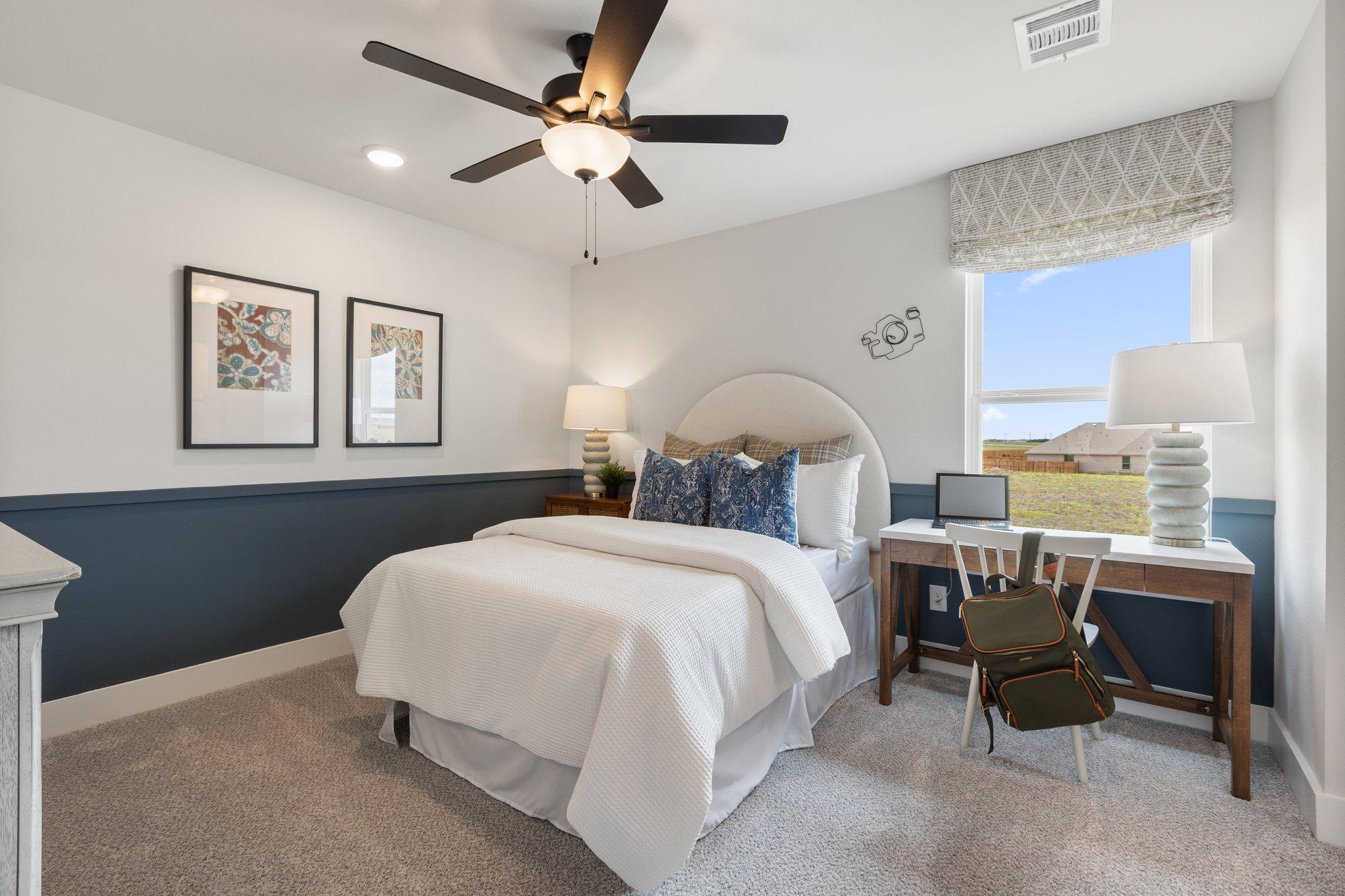 Spacious bedroom at Mercer Meadows in Royse City Texas with white bed, navy accent wall, wooden desk, ceiling fans, and field view