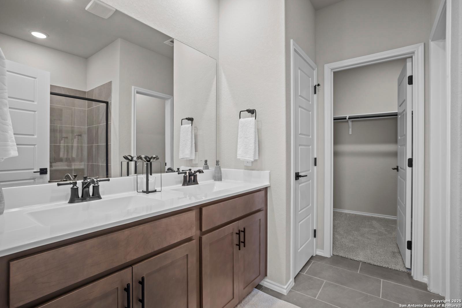 Modern master bathroom with double vanity, walk-in shower, and adjacent closet in Davidson Homes The Asheville H, Converse, TX