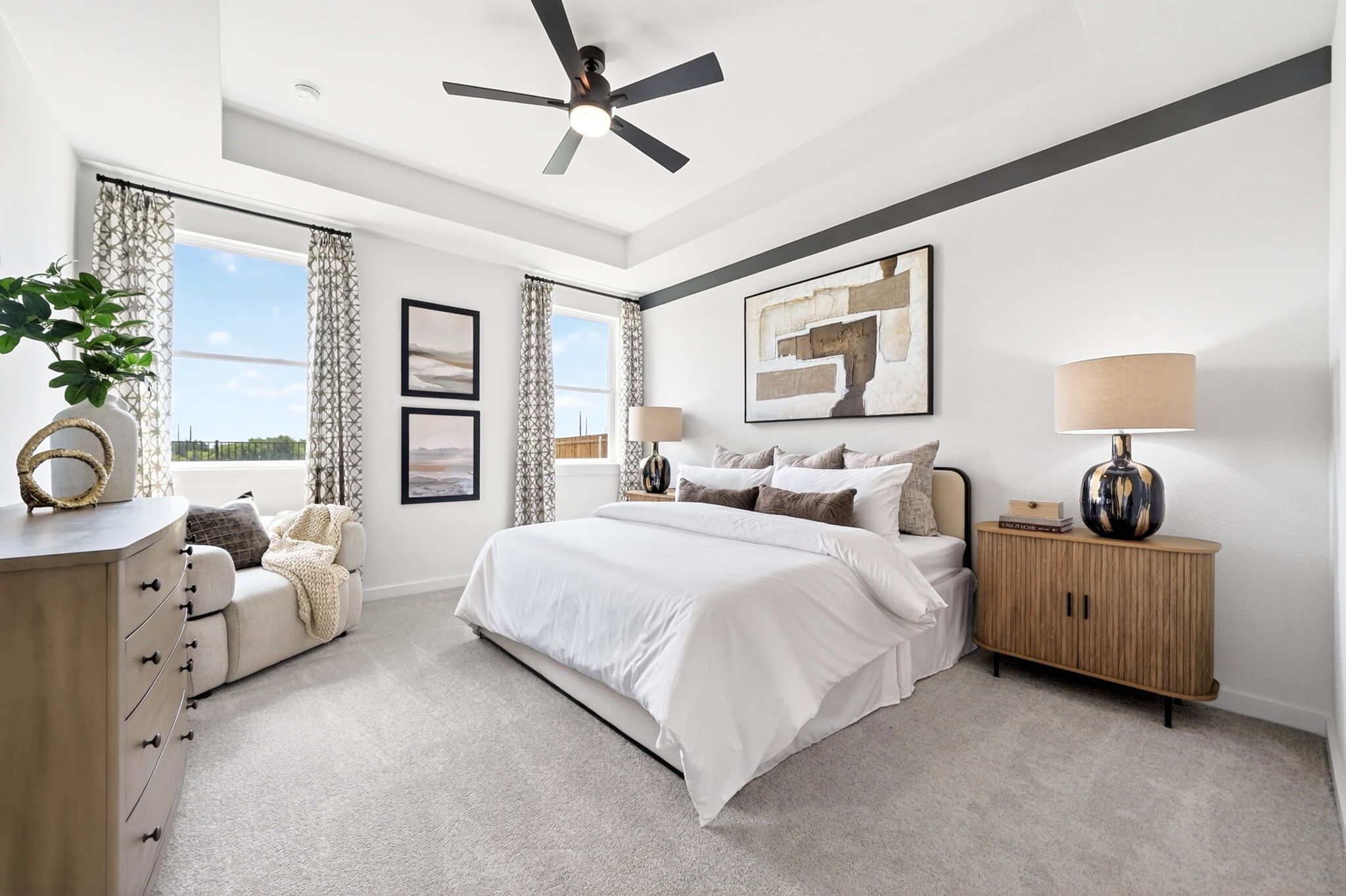 Modern primary bedroom in Parks at Foster Crossing by Davidson Homes with tray ceiling, cozy seating area, and neutral decor.