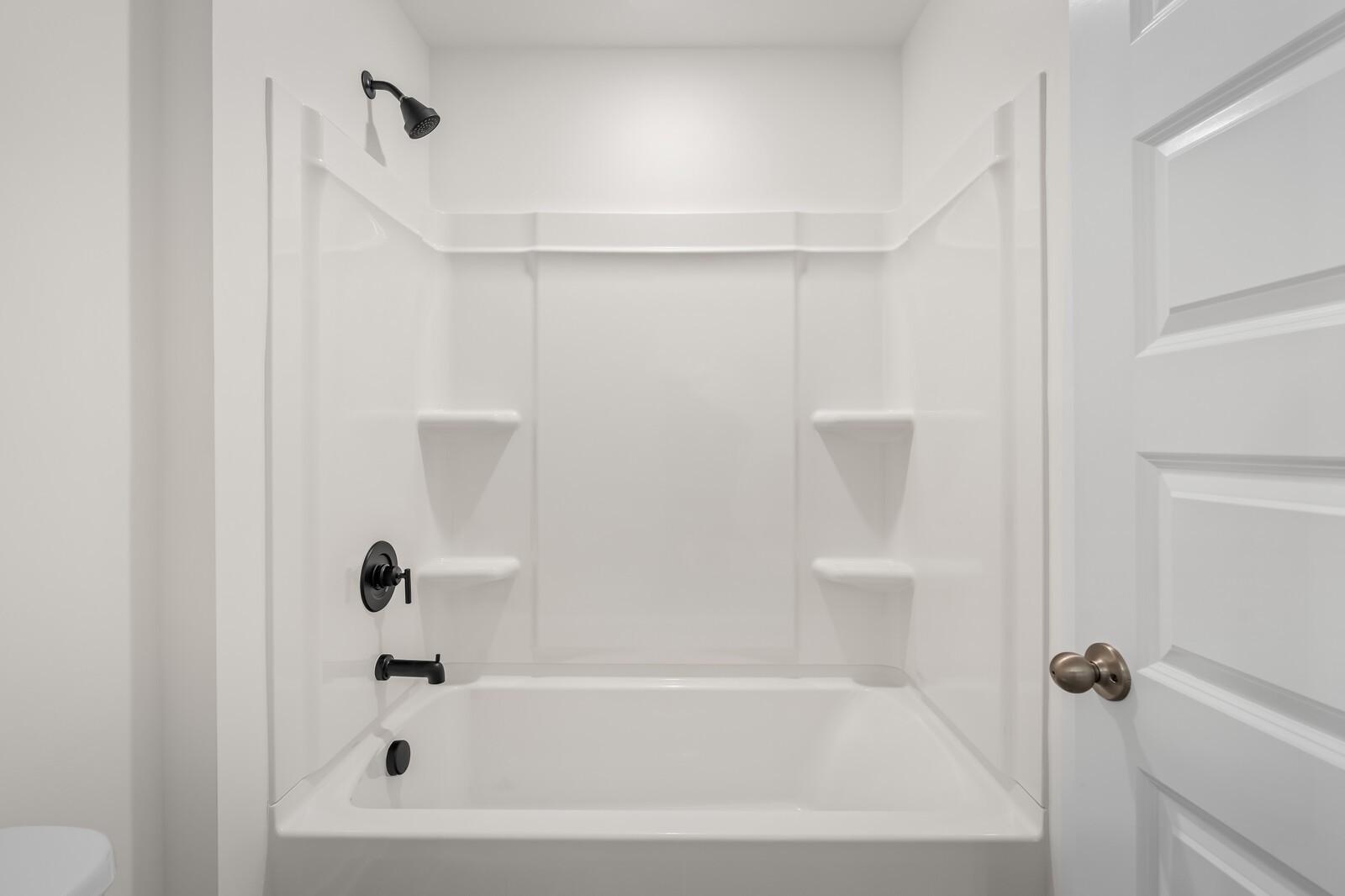 Bright white bathroom with tub-shower combo, black fixtures, and built-in shelves in Davidson Homes The Ash A, Gallatin, Tennessee