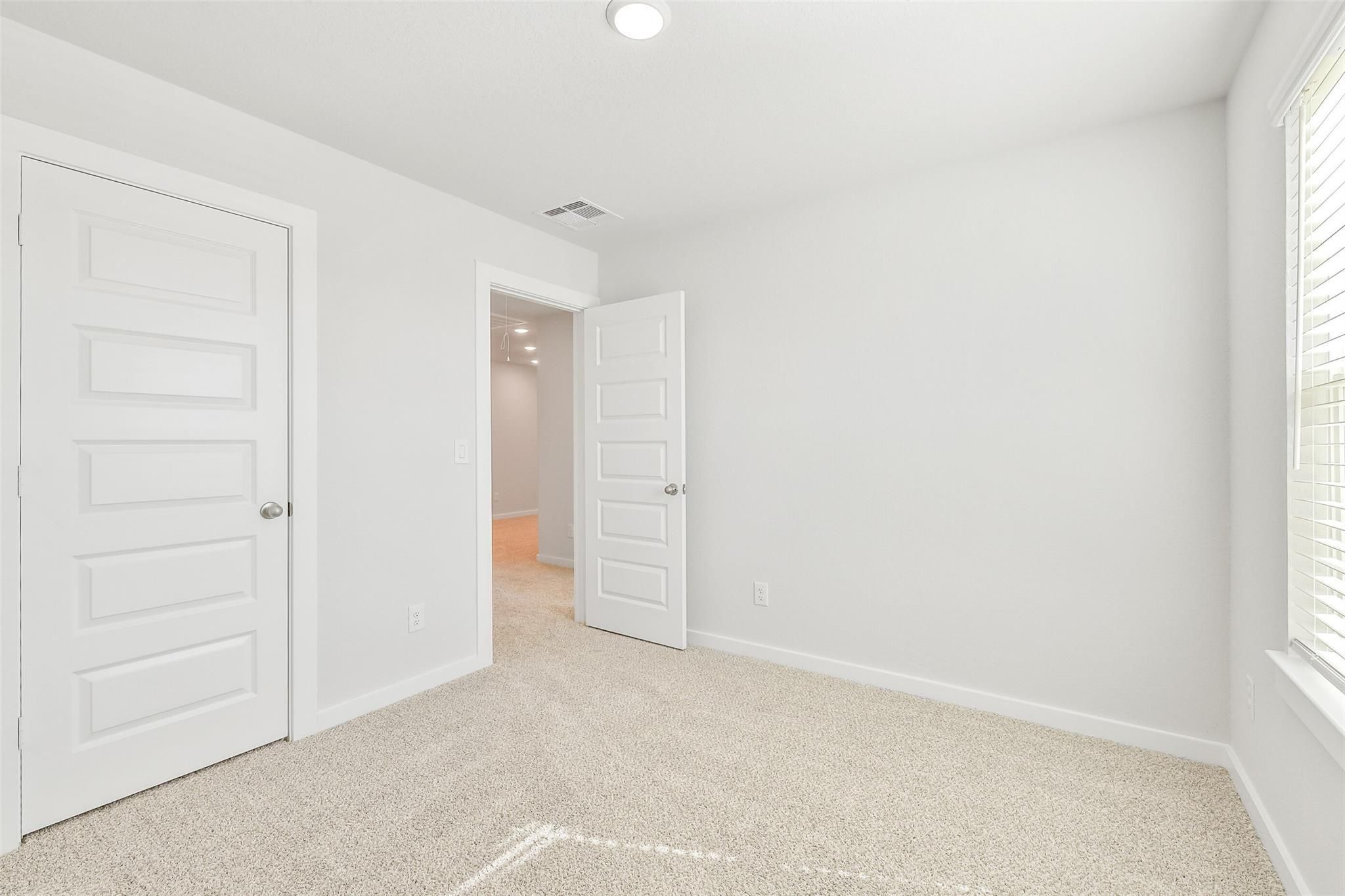 Bright secondary bedroom with white walls, beige carpet, double doors, and hallway access in Davidson Homes The Blanco E, Magnolia Texas