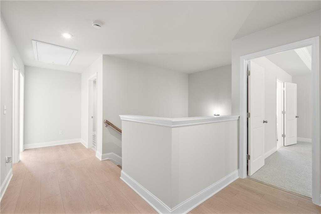 Bright upstairs hallway with light oak floors, white walls, open staircase railing, and bedroom doors in The Hickory B plan, Buford, GA