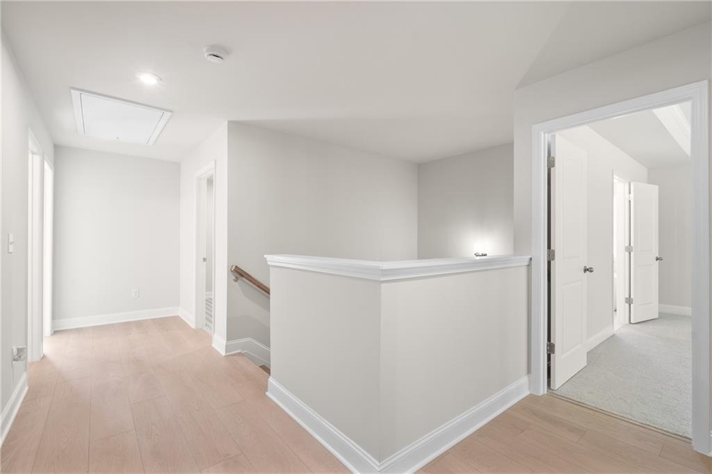 Bright upstairs hallway with oak laminate floors, white walls, and open doors in The Hickory E by Davidson Homes, Buford, GA