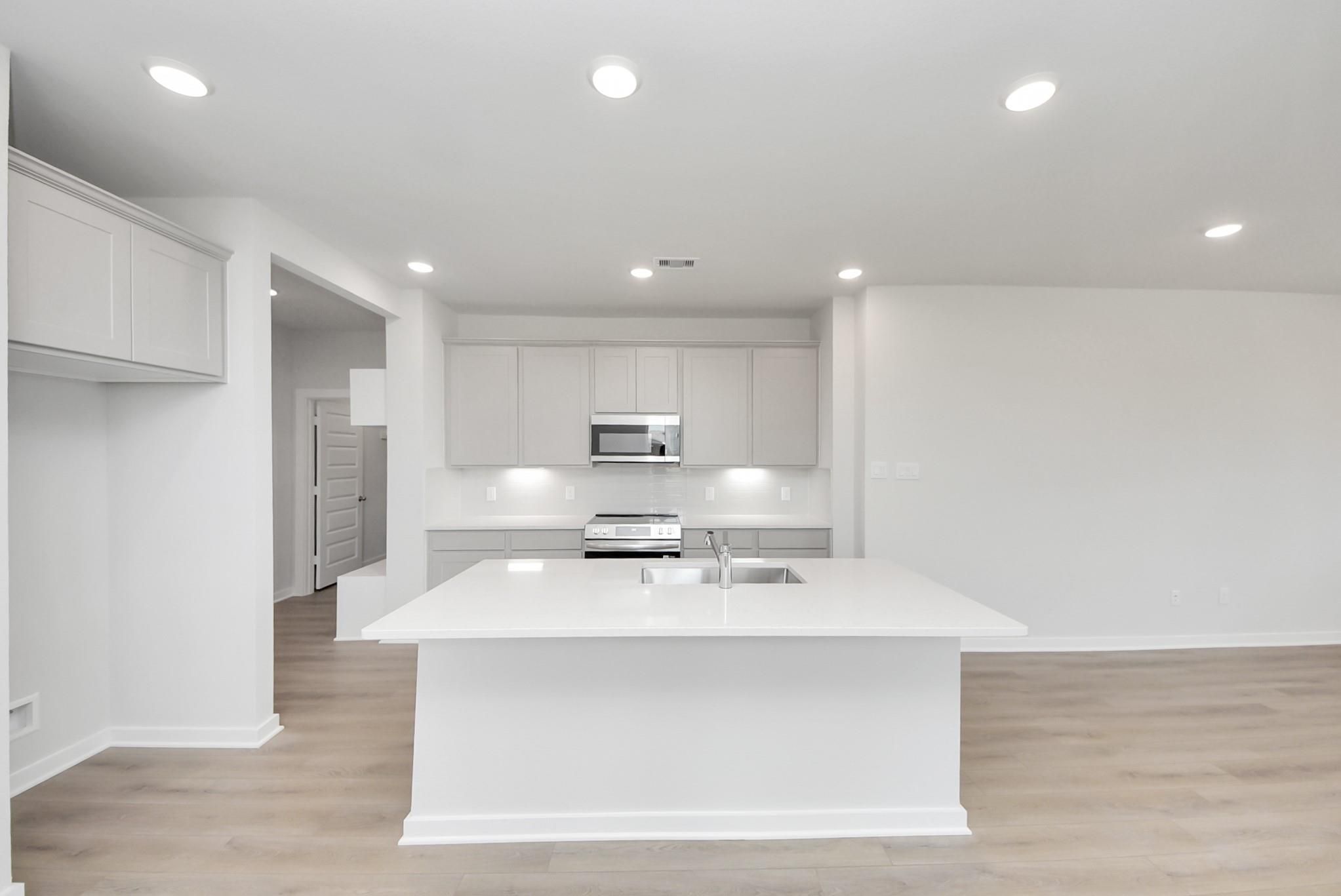 Modern kitchen with large white island, stainless appliances, and gray cabinetry in The Blanco F at Spring Branch Crossing.