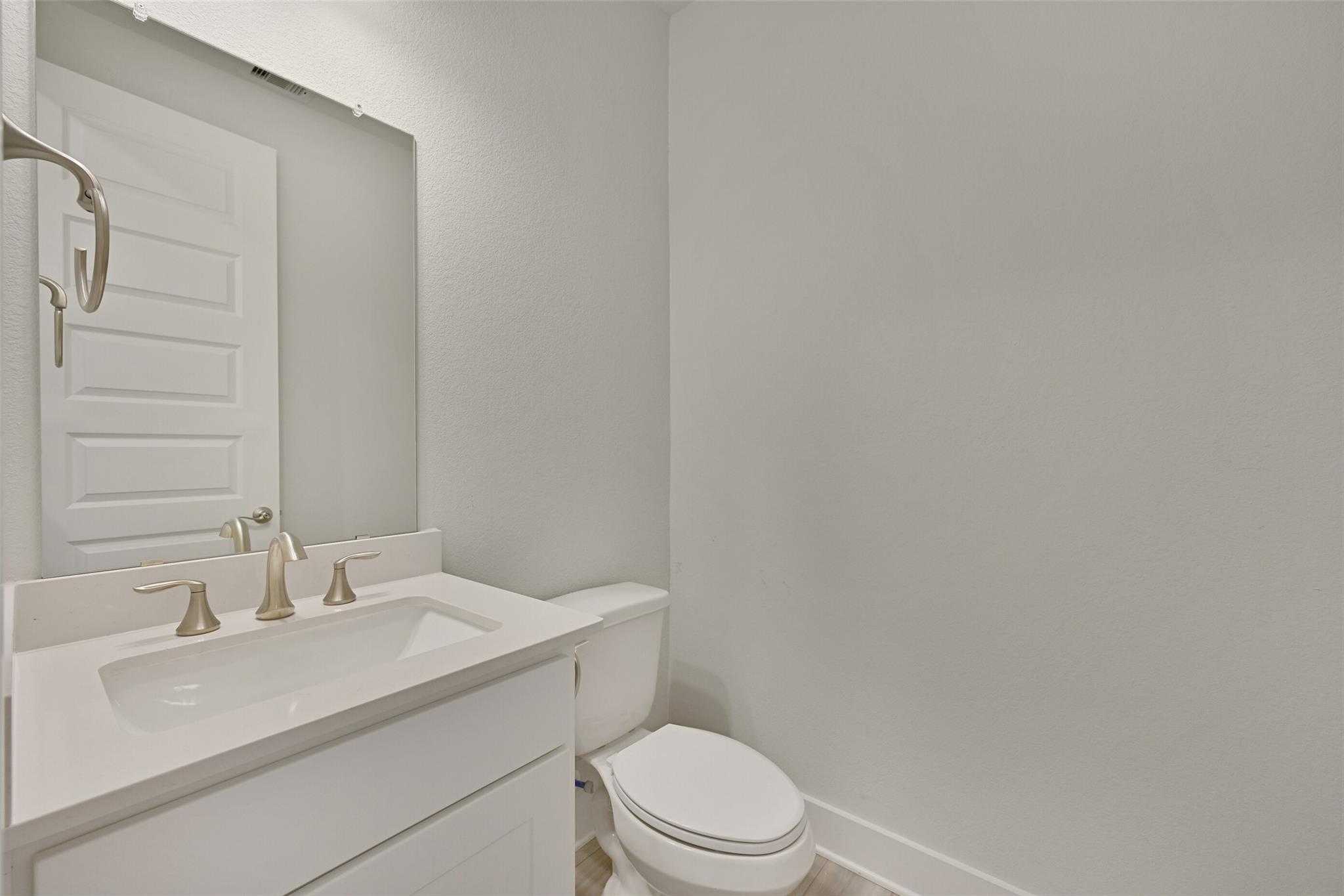 Modern powder room with white quartz vanity, chrome faucet, mirror, and toilet in Davidson Homes The Edward A, Lago Mar, Texas City