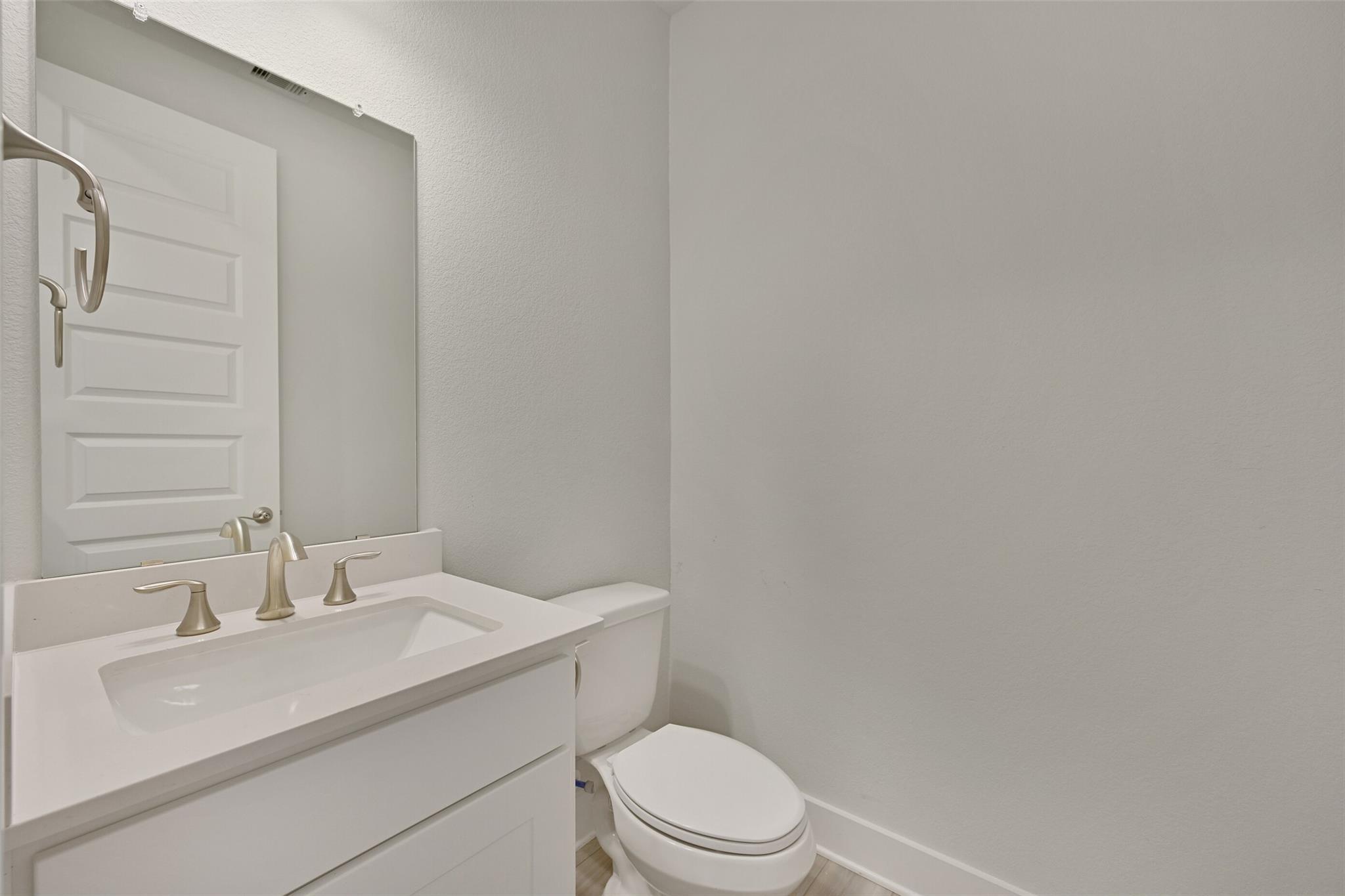 Modern powder room with white quartz vanity, chrome faucet, mirror, and toilet in Davidson Homes The Edward A, Lago Mar, Texas City