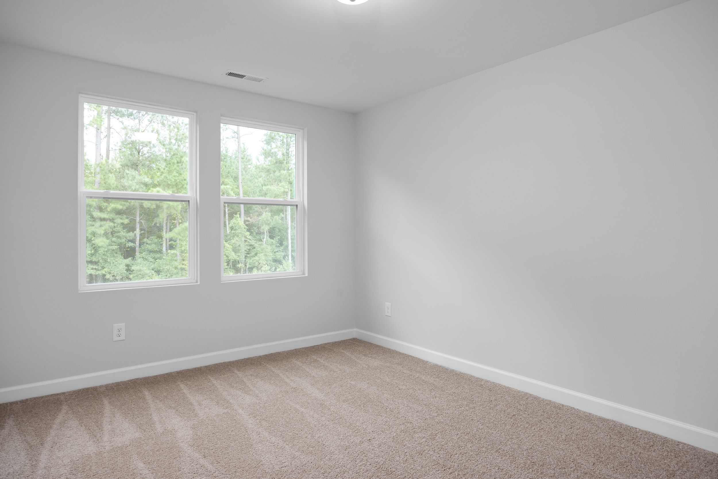 Bright bedroom interior with neutral carpet and windows overlooking trees in The Warren floor plan by Davidson Homes.