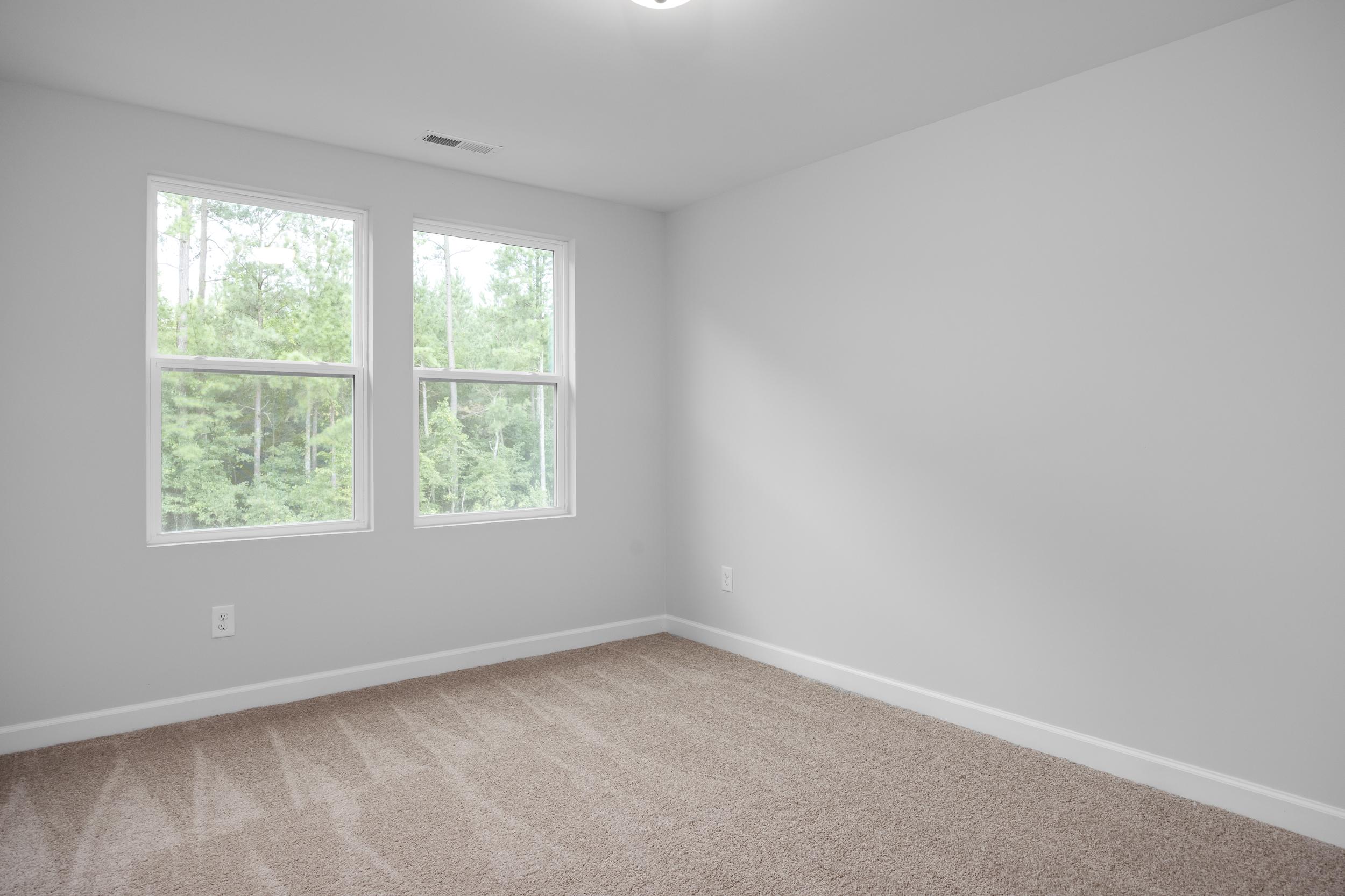 Bright bedroom interior with neutral carpet and windows overlooking trees in The Warren floor plan by Davidson Homes.