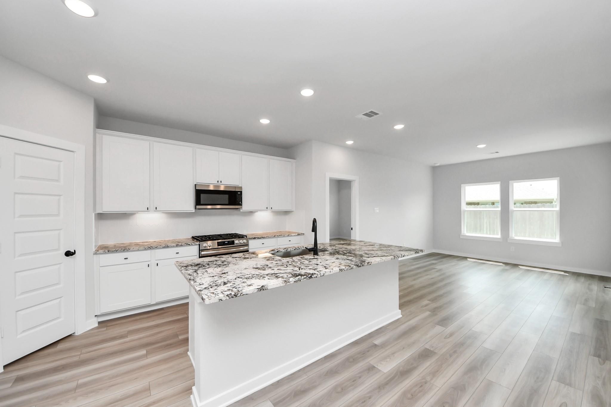 Modern kitchen with white cabinets, granite island, and wood-look flooring in The Everett C floor plan, Dayton, Texas.