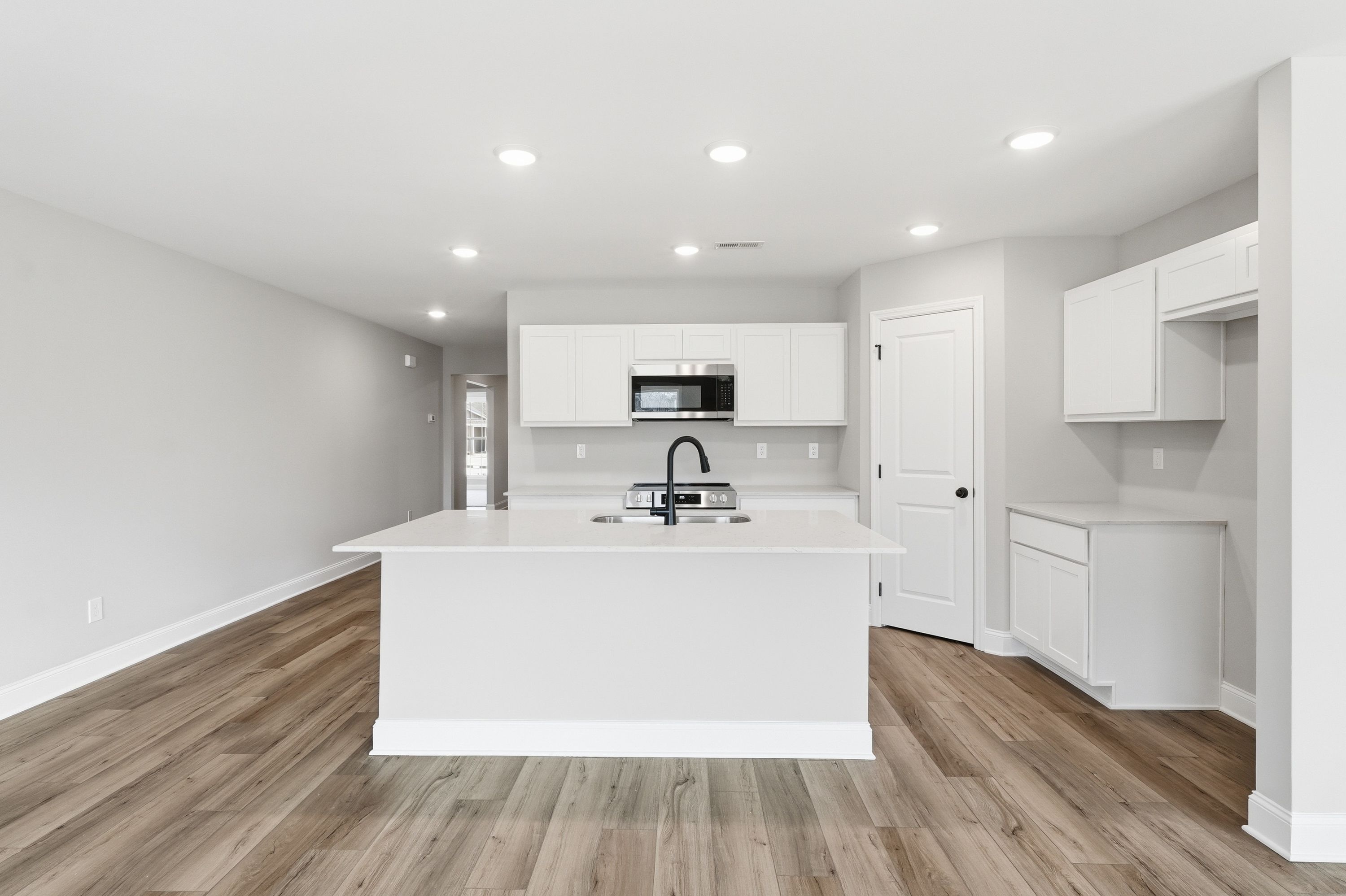 Spacious modern kitchen in The Daphne V with white shaker cabinets, large island sink, stainless appliances, and wood flooring
