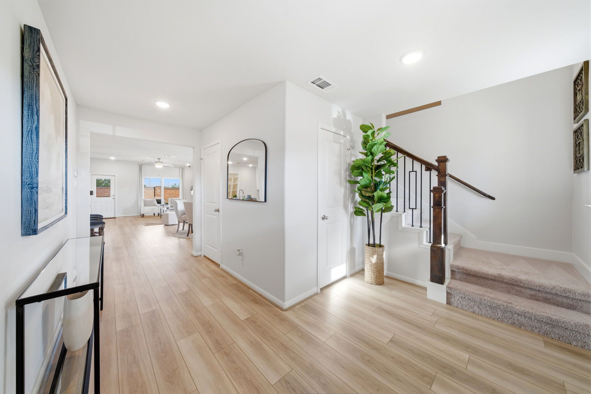 Spacious hallway in Sunterra Katy Texas home by Davidson Homes with light wood floors, potted plant, and black metal staircase