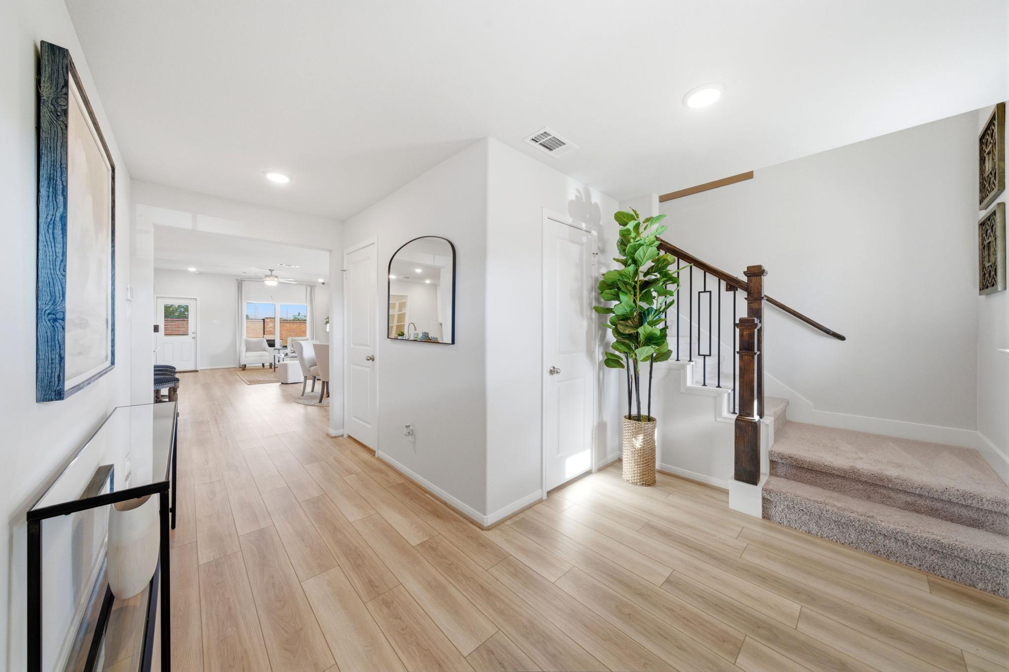 Spacious hallway in Sunterra Katy Texas home by Davidson Homes with light wood floors, potted plant, and black metal staircase