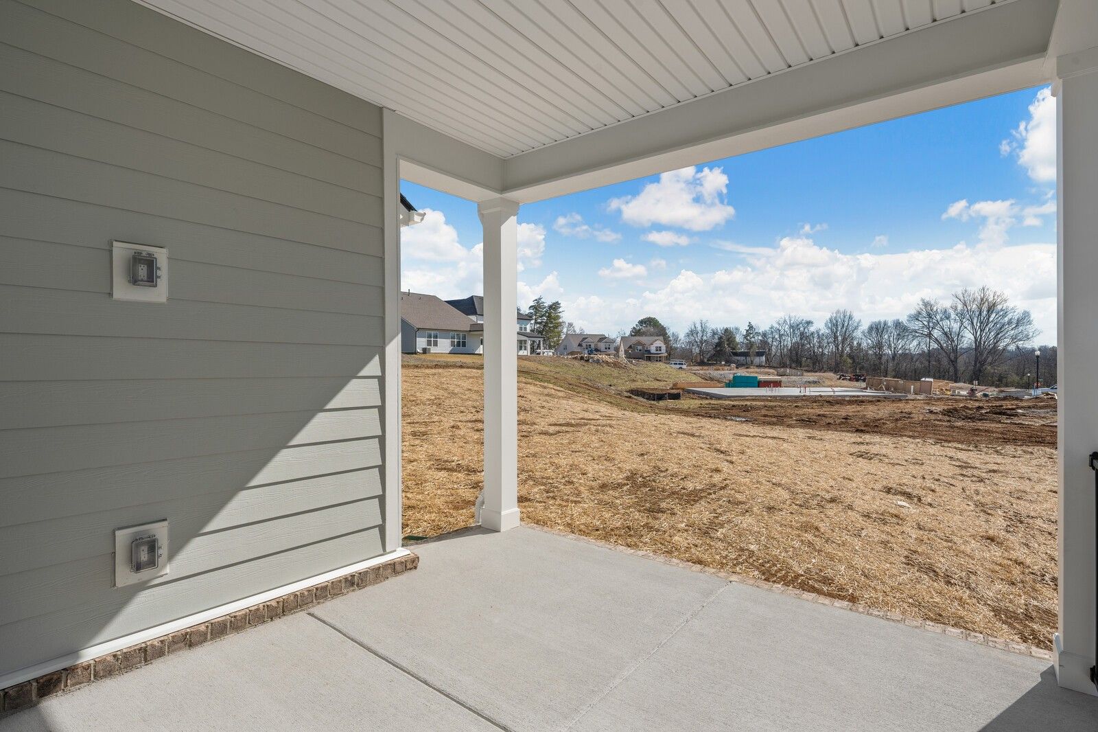 Covered porch with gray siding and white columns overlooking open field in Davidson Homes The Ash A, Gallatin, Tennessee