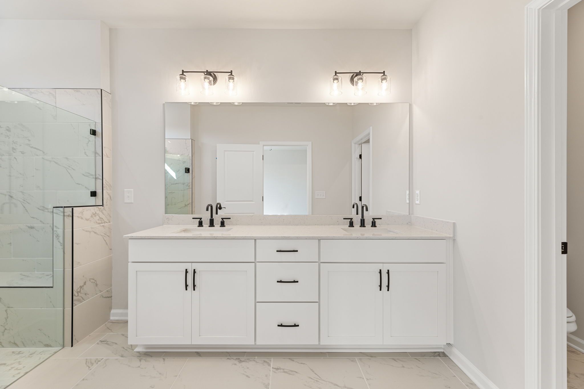 Elegant master bathroom with white double vanity, marble counters, and glass shower in The Glenwood C, Davidson Homes, Loganville GA