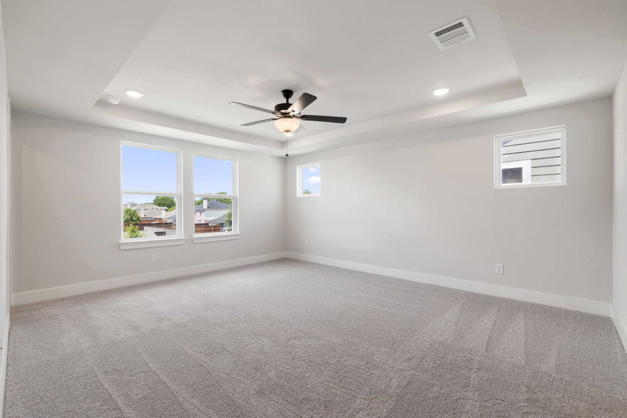 Bright bedroom with tray ceiling, ceiling fan, large windows, and neutral carpet in The Durham E by Davidson Homes, Wylie, Texas