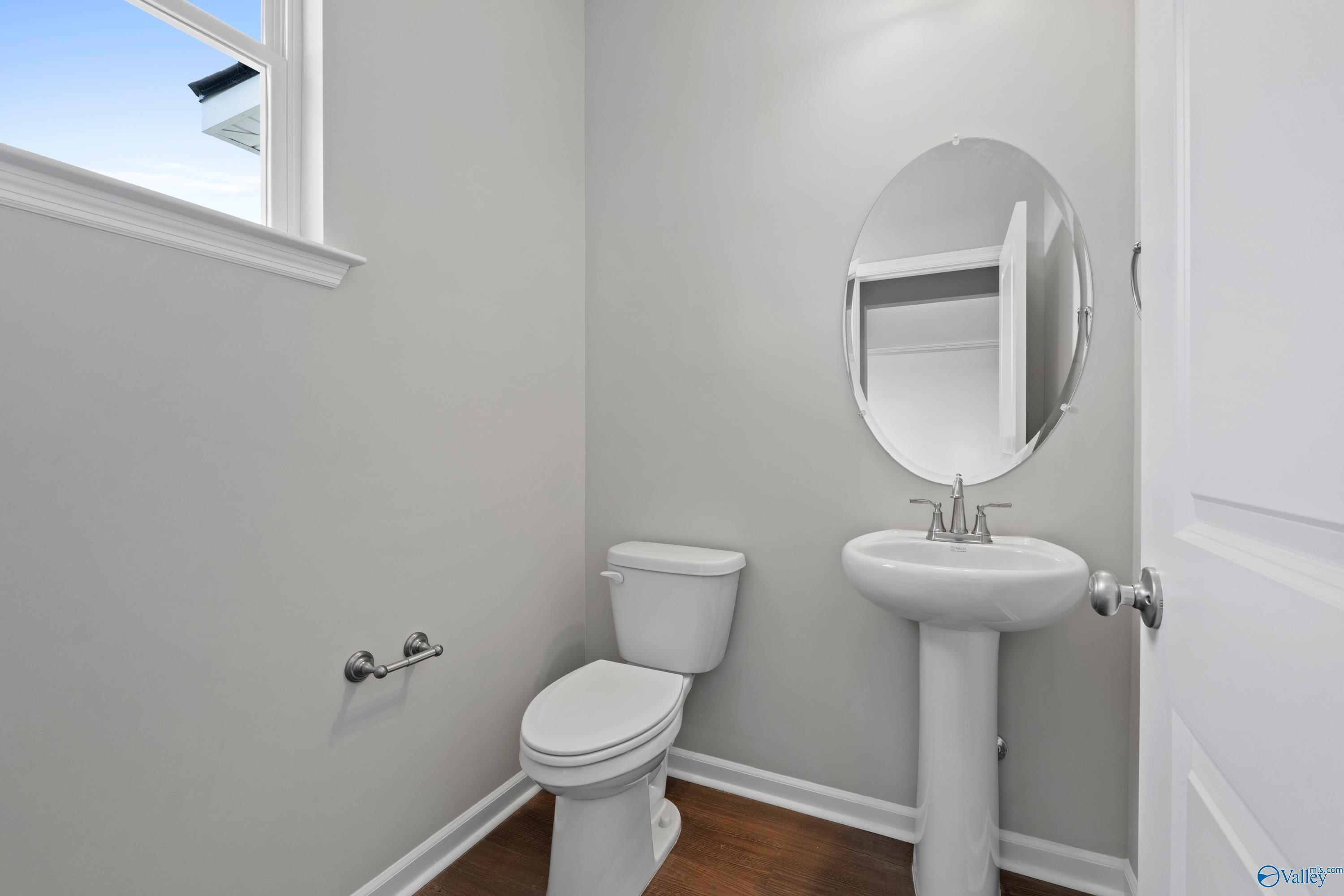 Modern powder room with white pedestal sink, oval mirror, gray walls, and wood floors in Davidson Homes The Dorado, Athens AL