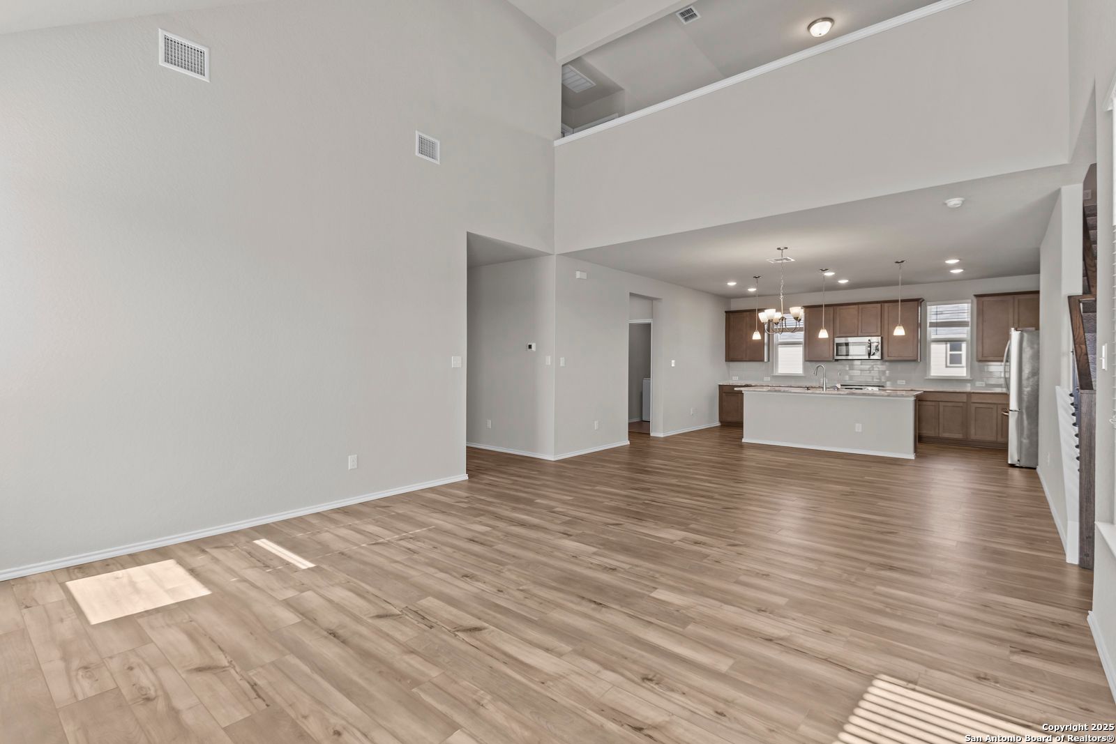 Open-concept kitchen with white cabinets, island, stainless appliances and hardwood floors in The Collin B, Seguin, Texas