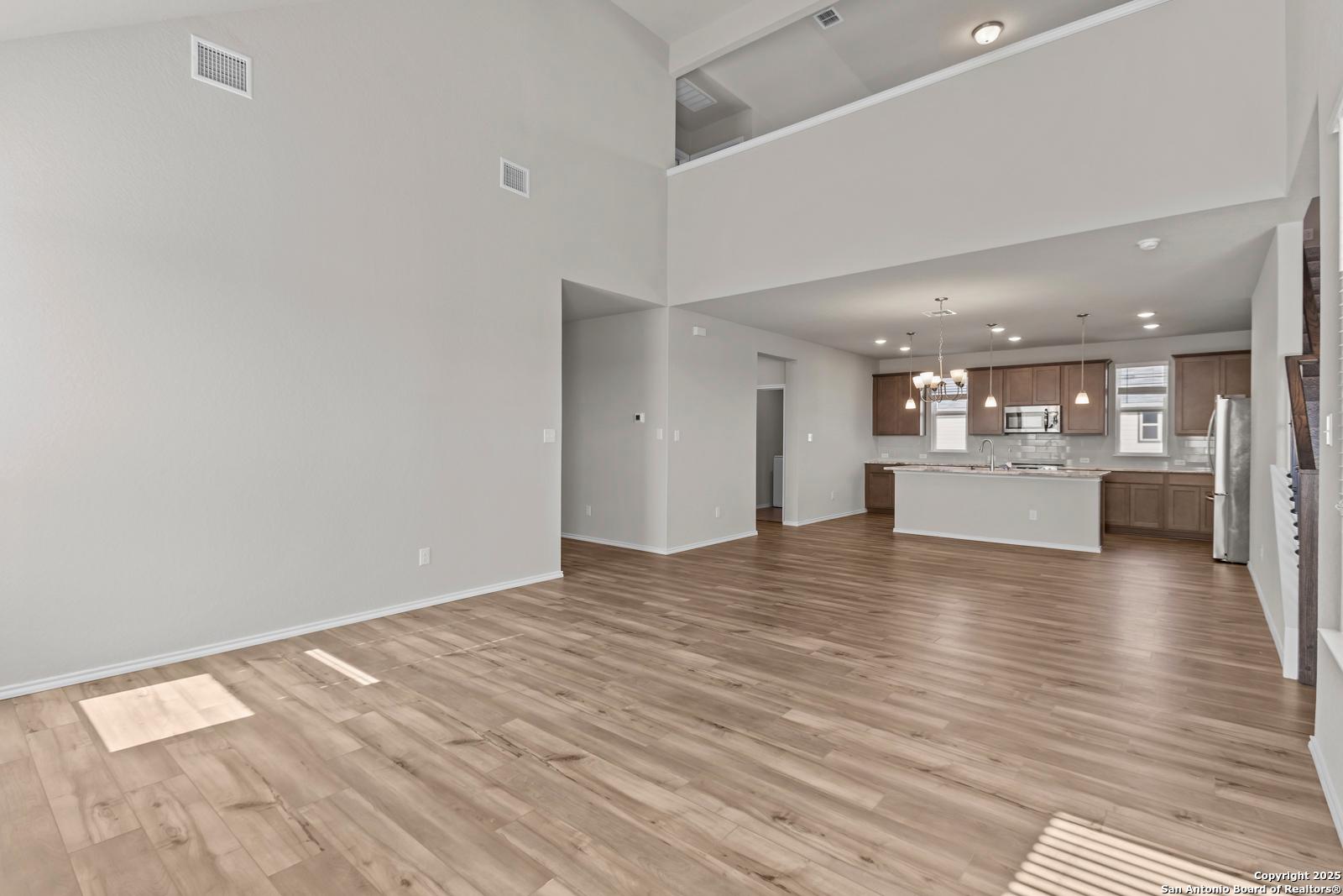Open-concept kitchen with white cabinets, island, stainless appliances and hardwood floors in The Collin B, Seguin, Texas