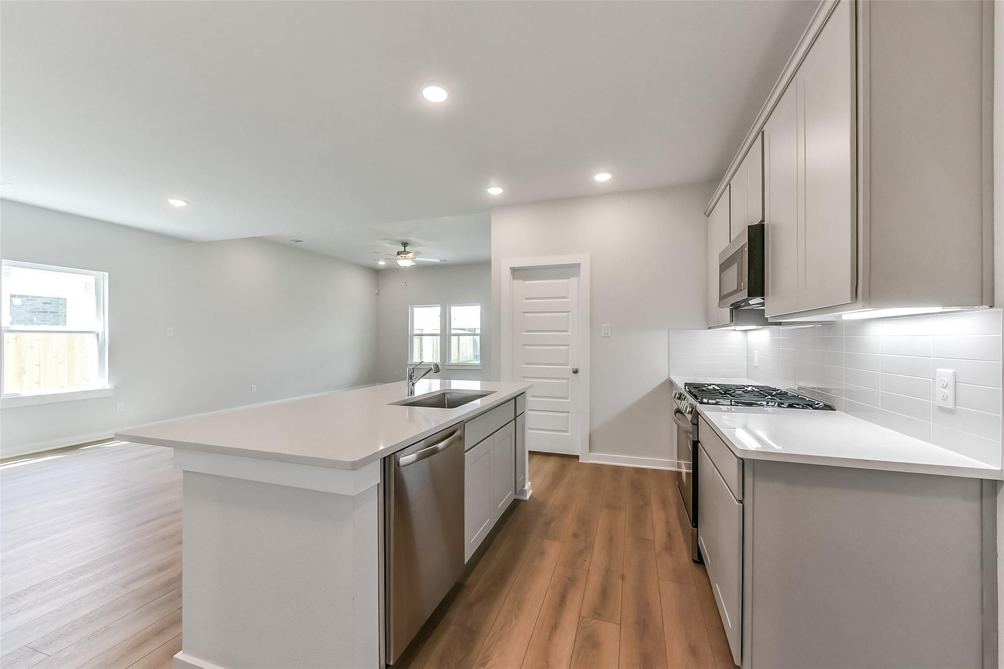 Contemporary kitchen with white quartz island sink, stainless dishwasher, gray shaker cabinets, subway tile backsplash in Davidson Homes The Tierra C, Dayton, Texas