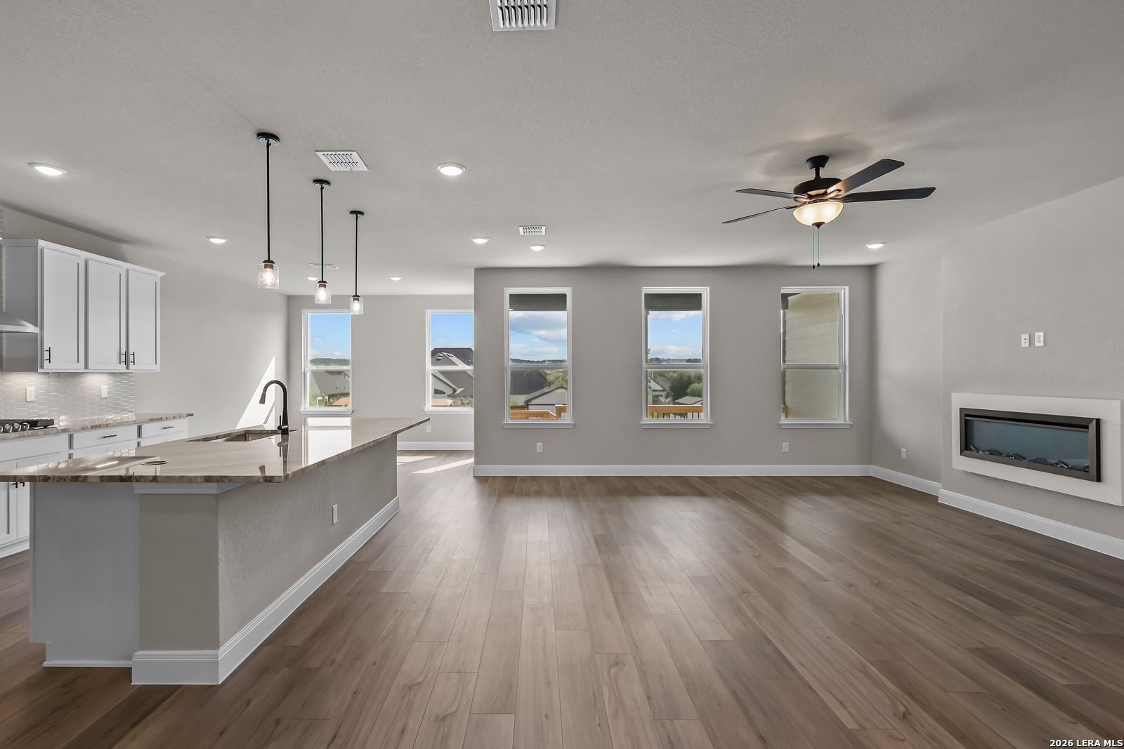 Open-concept living area with kitchen island, wood-look flooring, and linear fireplace in Davidson Homes The Foster E, Castroville