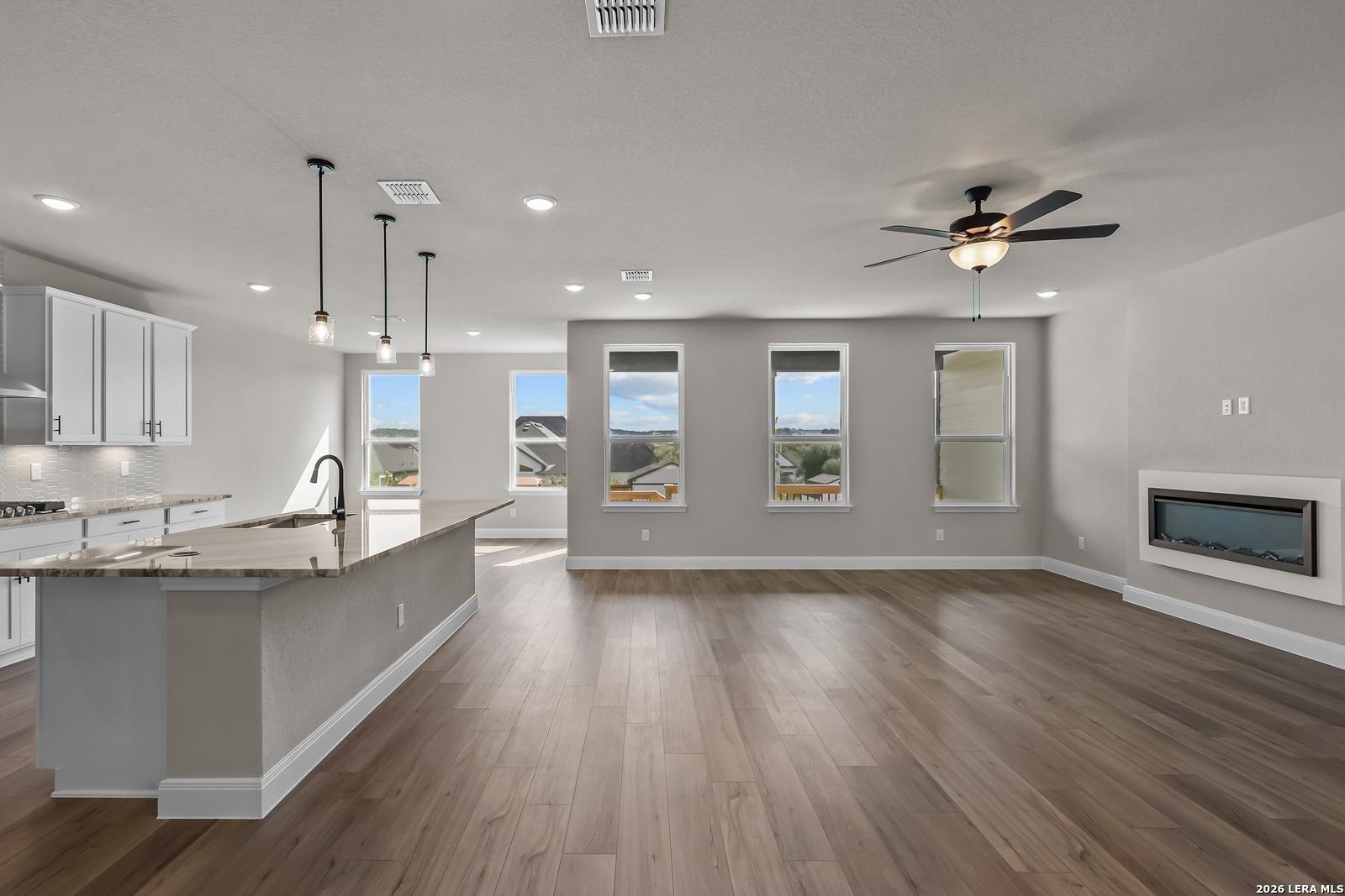 Open-concept living area with kitchen island, wood-look flooring, and linear fireplace in Davidson Homes The Foster E, Castroville