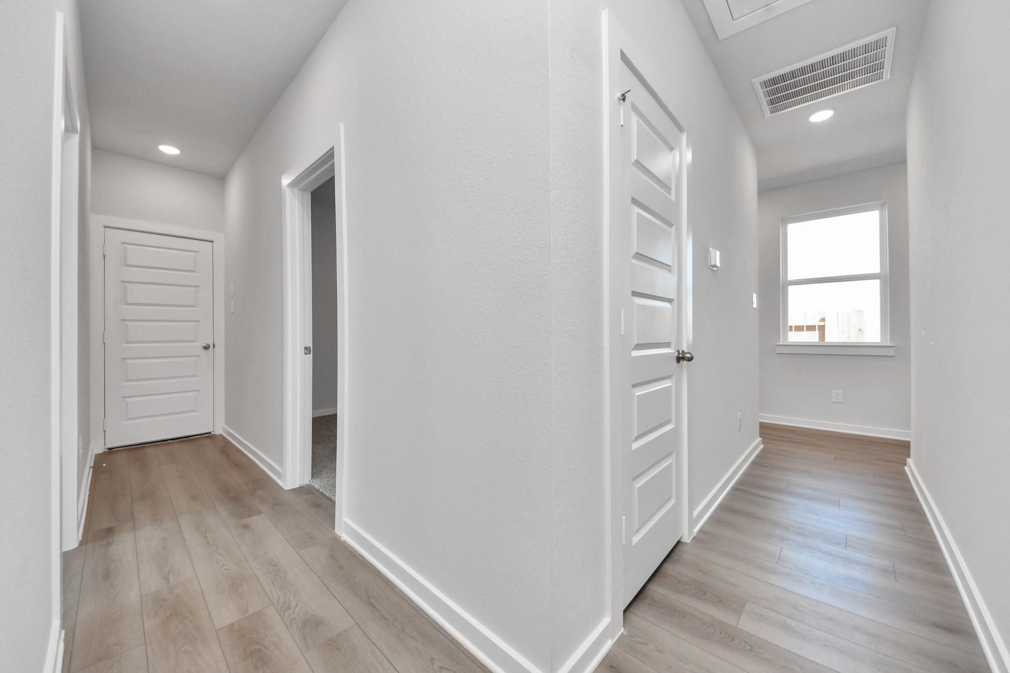 Bright, modern hallway with wood-style flooring in The Colorado G floor plan by Davidson Homes in Emberly, Beasley, Texas.