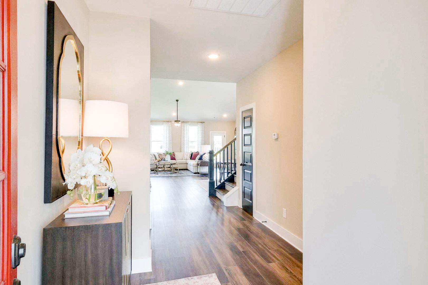 Elegant entryway at The Meadows in Smyrna TN by Davidson Homes with hardwood floors, gold mirror, floral vase, and open living room view