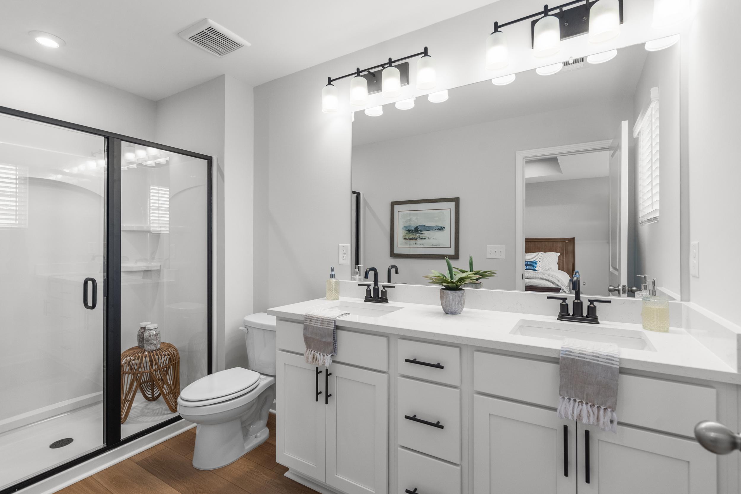 Modern primary bathroom at Stegall Village in Emerson, Georgia with double white vanity, frameless glass shower, and sleek black fixtures