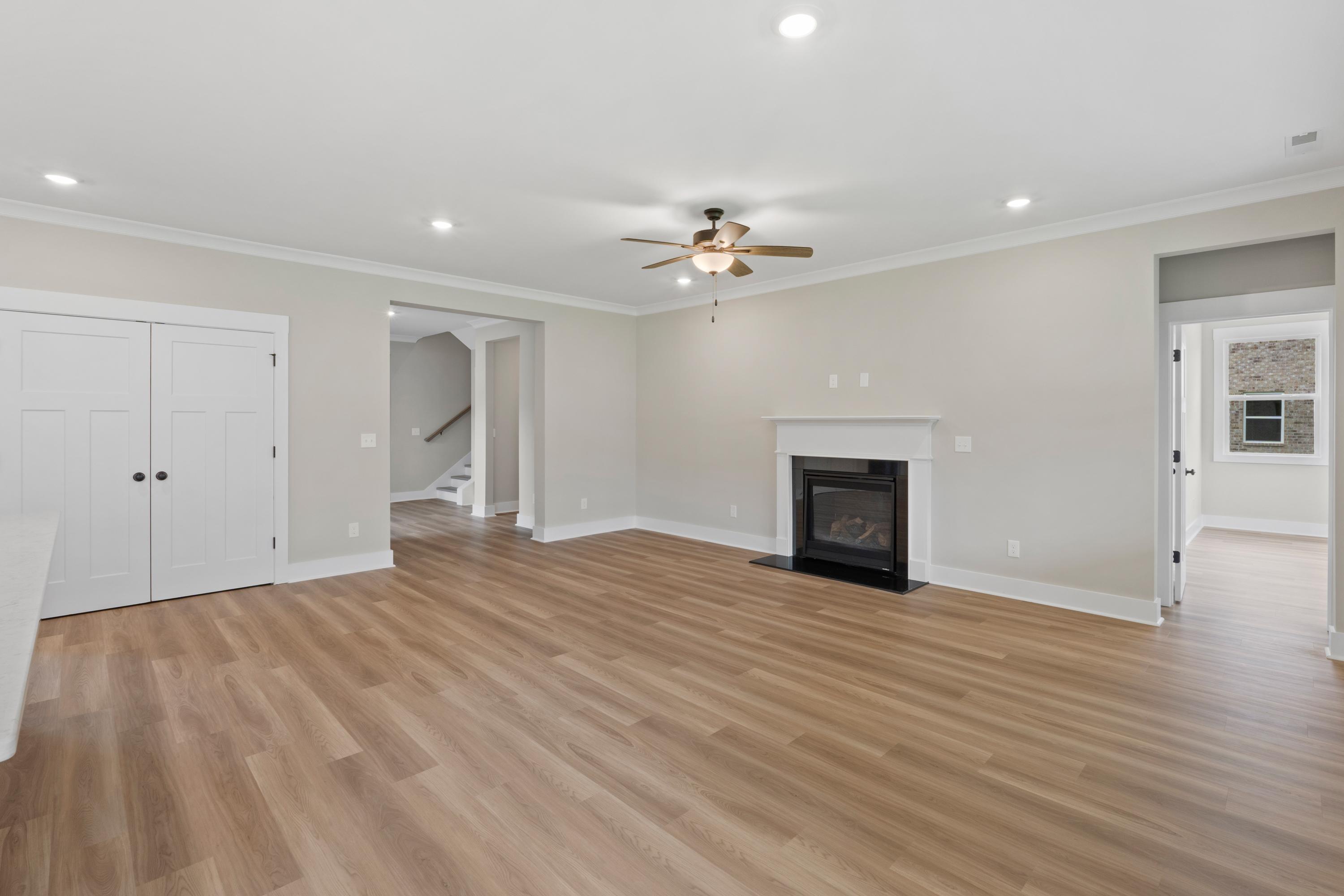 Spacious living room in The Oxford B with modern gas fireplace, ceiling fan, arched staircase entry, and luxury vinyl plank floors