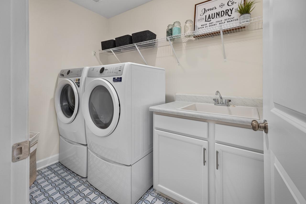 Laundry room in The Wake floor plan featuring white cabinets, utility sink, wire shelving, and modern tile flooring.