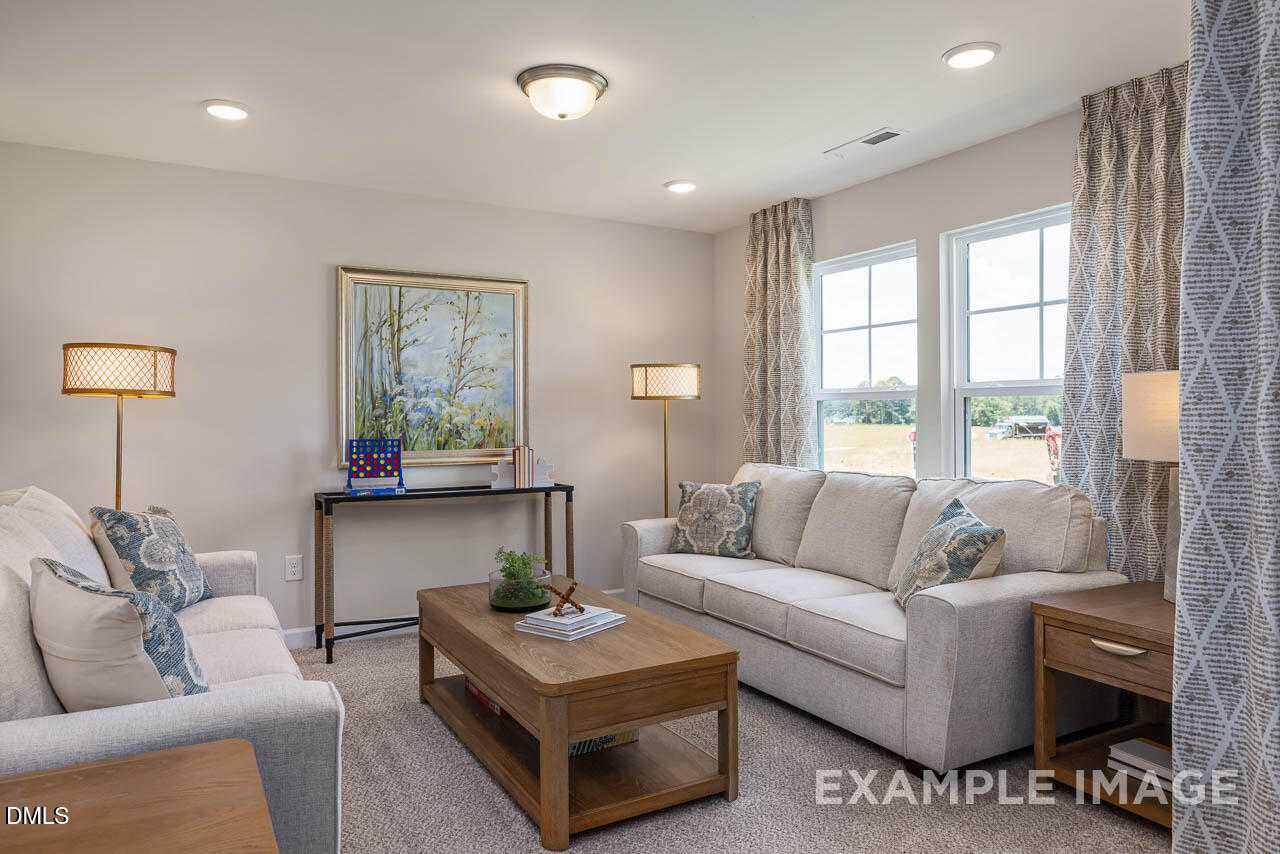 Cozy living room with beige sofas, wooden coffee table, lamps, and large windows in Davidson Homes The Willow B, Lillington, NC