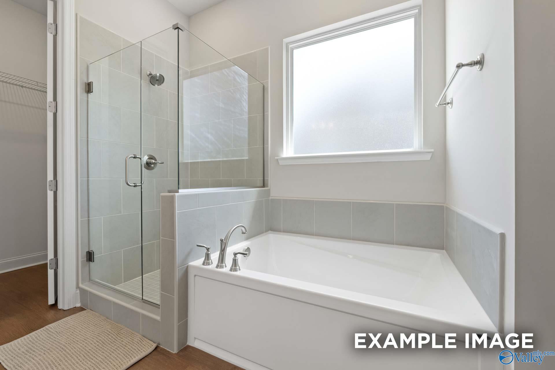 Elegant master bathroom with glass shower enclosure, corner soaking tub, and frosted window in Evermore Homes The Haven E, Owens Cross Roads, Alabama