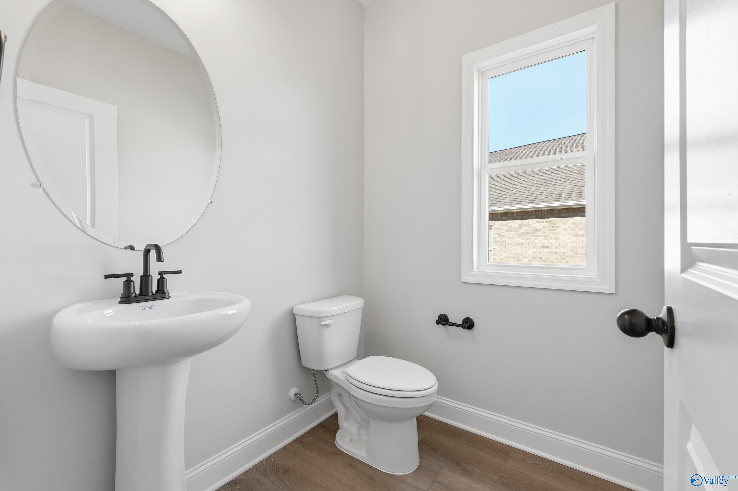 Elegant powder room featuring white pedestal sink, round mirror, and window in Davidson Homes The Chelsea C, Harvest, Alabama
