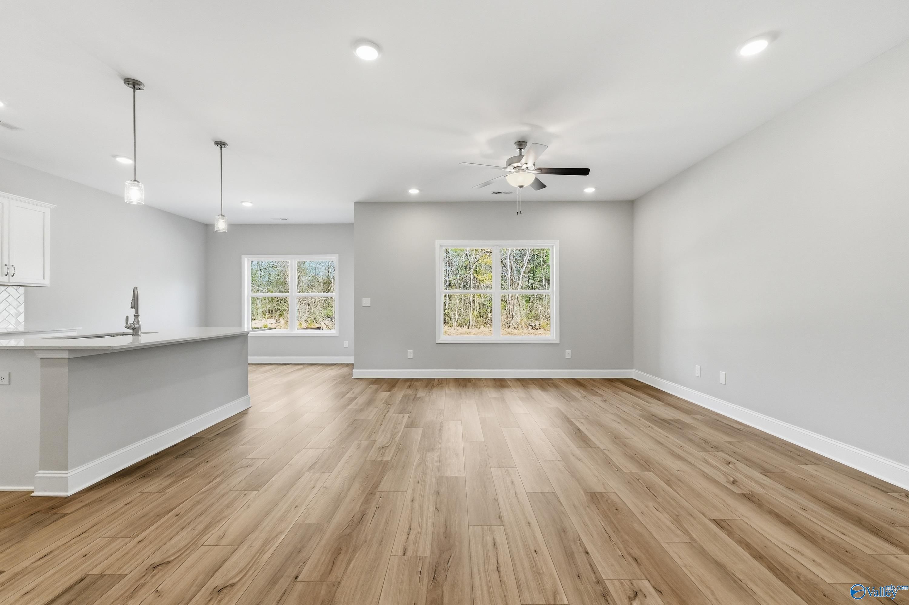 Open-concept kitchen and living area with hardwood floors, gray walls, large windows, and ceiling fan in The Asheville floor plan, Huntsville AL
