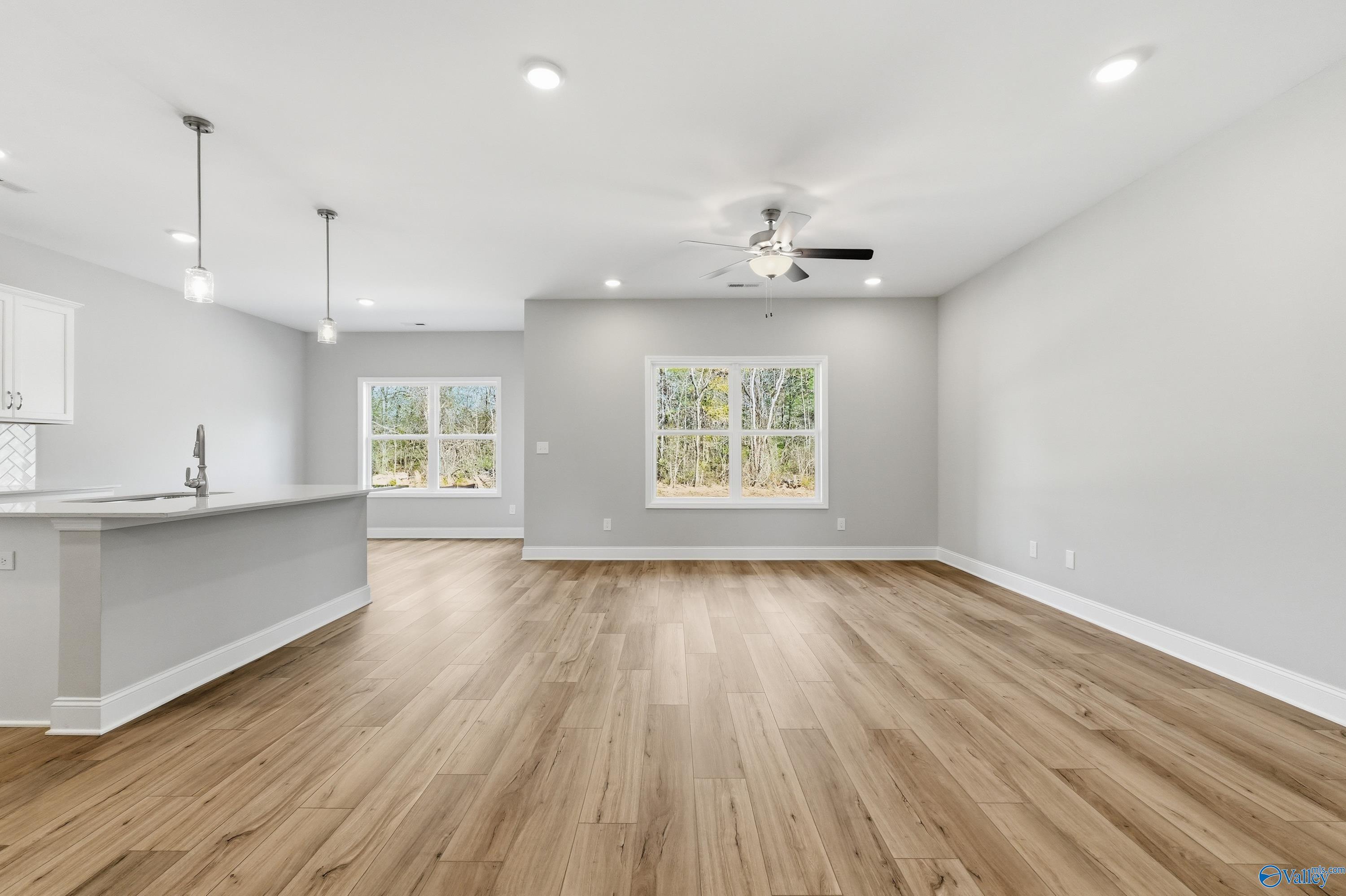 Open-concept kitchen and living area with hardwood floors, gray walls, large windows, and ceiling fan in The Asheville floor plan, Huntsville AL