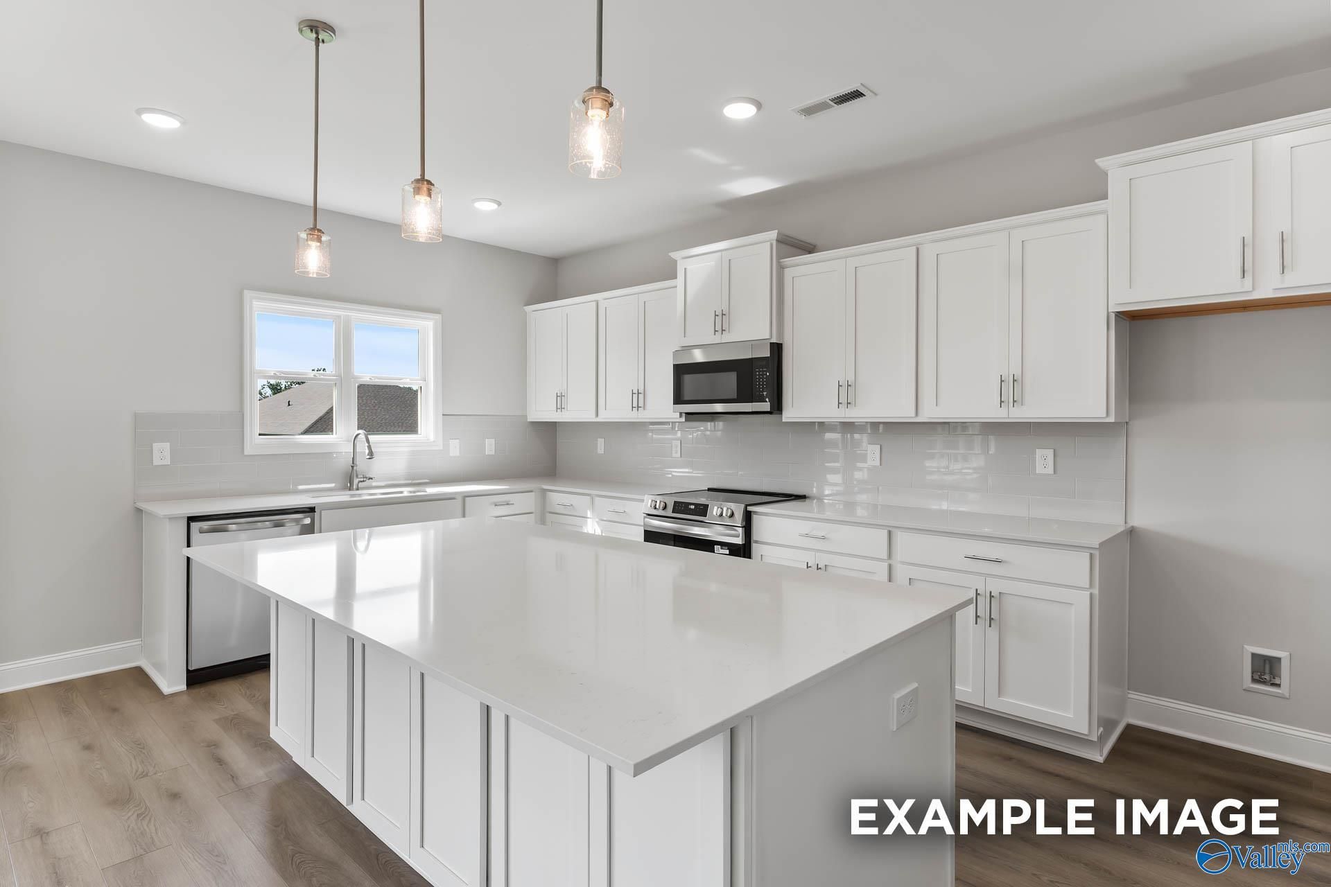 Spacious white kitchen with quartz island, stainless appliances, pendant lights in Davidson Homes Chelsea D, New Market AL