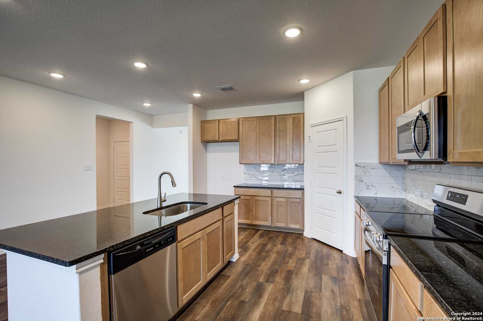 Modern kitchen with oak cabinets, black granite island, stainless steel appliances in Davidson Homes The Douglas D, Seguin, Texas