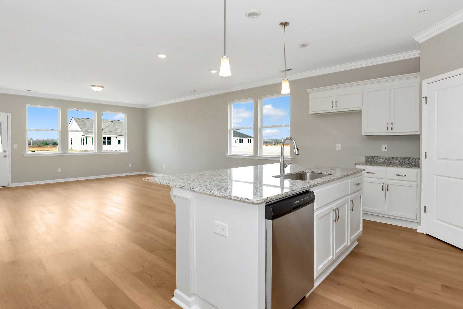 Spacious open-concept kitchen at Links Crossing in Auburn AL with white cabinetry, granite island, hardwood floors, and large windows