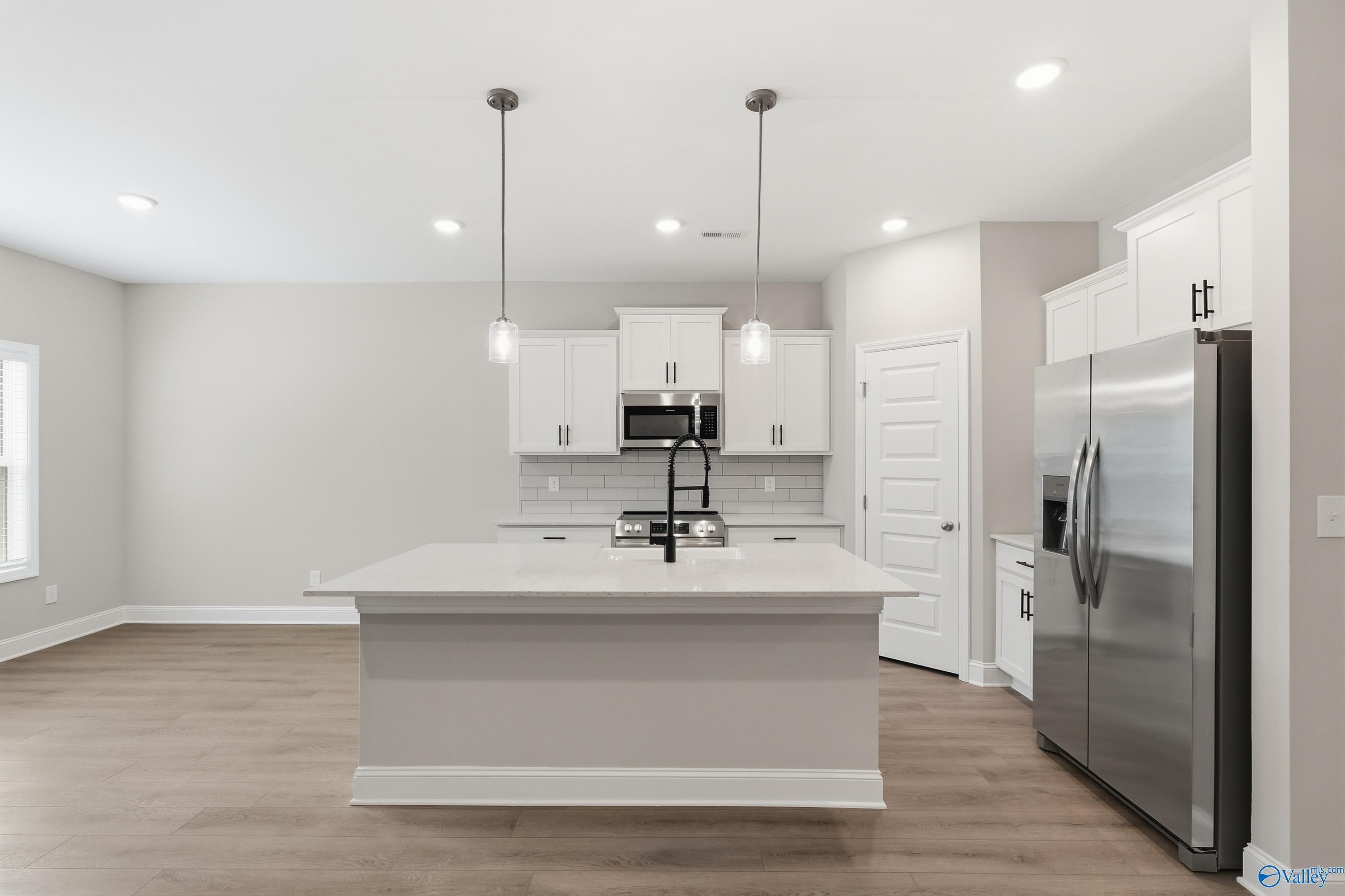 Modern white kitchen with stainless steel appliances, large center island, and pendant lights in Davidson Homes The Asheville C, Arab, Alabama