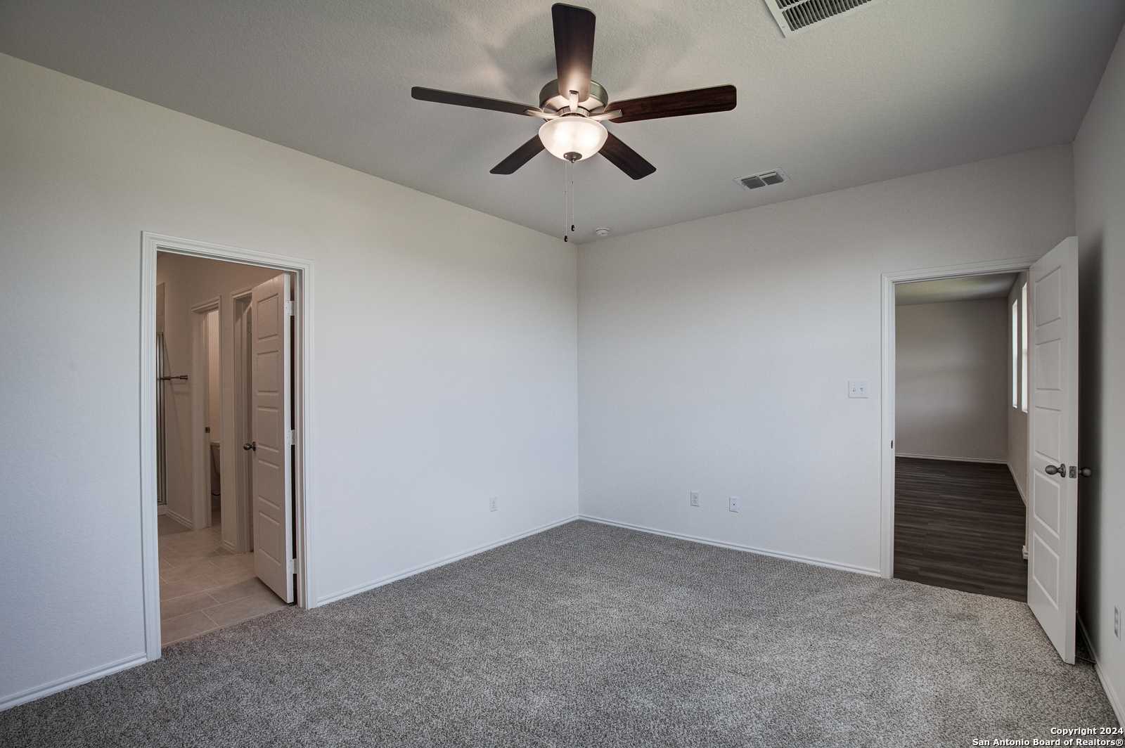 Spacious master bedroom with ceiling fan, carpeted floors, and en-suite bath in Davidson Homes The Douglas D, Seguin, Texas