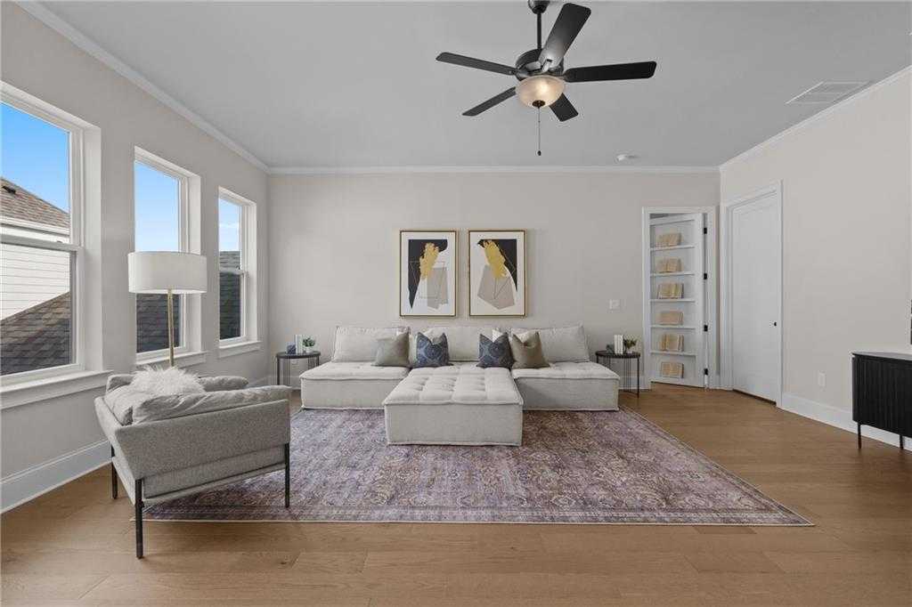 Cozy living room with beige L-shaped sofa, armchair, ceiling fan, abstract art, and hardwood floors in Davidson Homes The Seaside B, Woodstock, GA